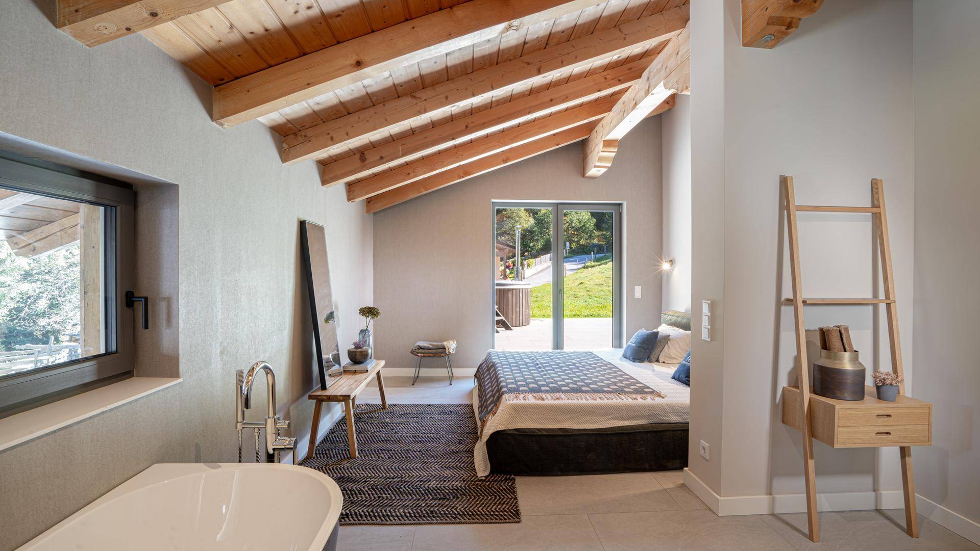 Schlafzimmer mit freistehender Badewanne, Holzbalkendecke und Zugang zum Außenbereich.