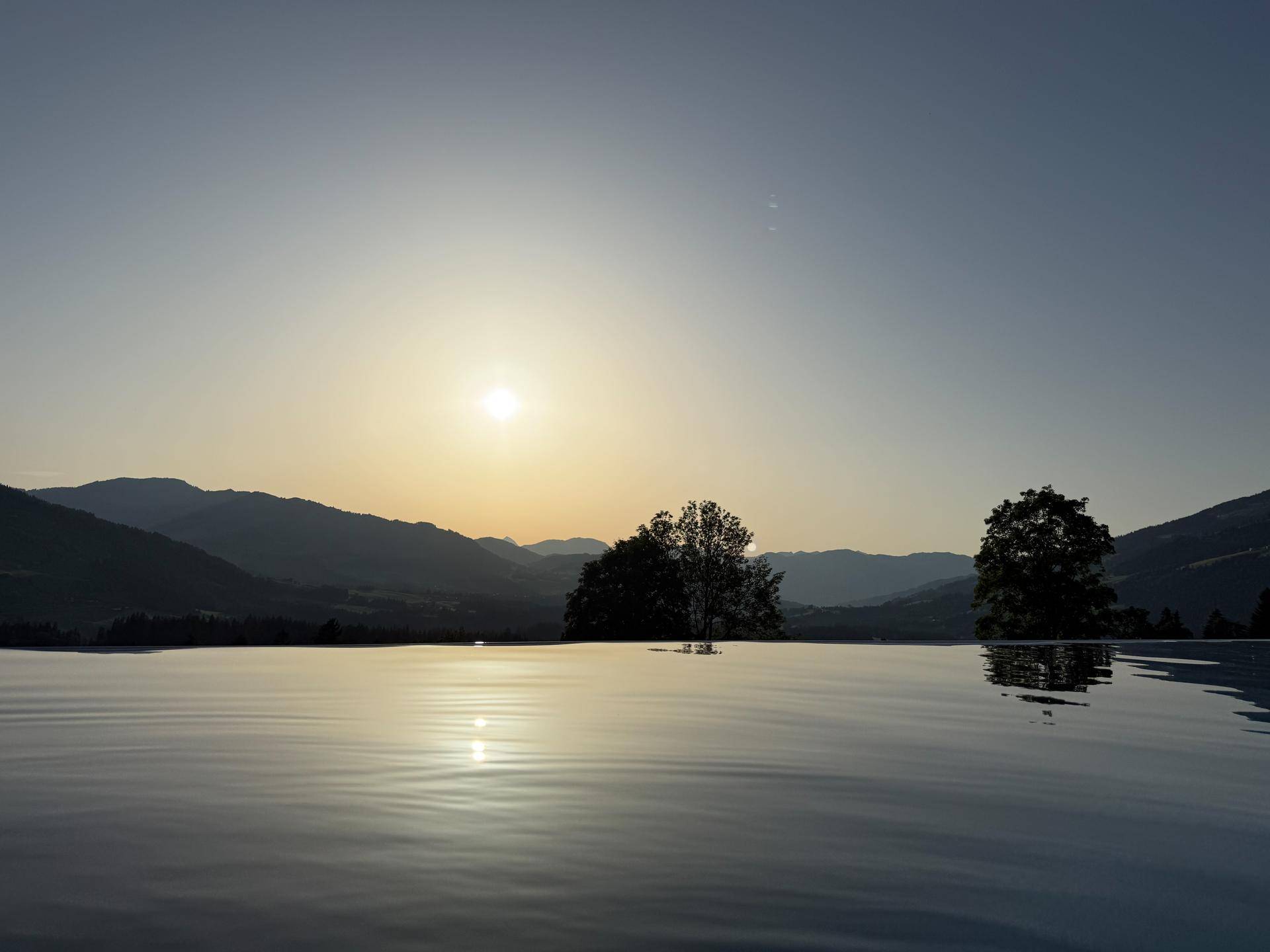 Infinity-Pool bei Sonnenuntergang mit ruhiger Wasseroberfläche und Bergpanorama.
