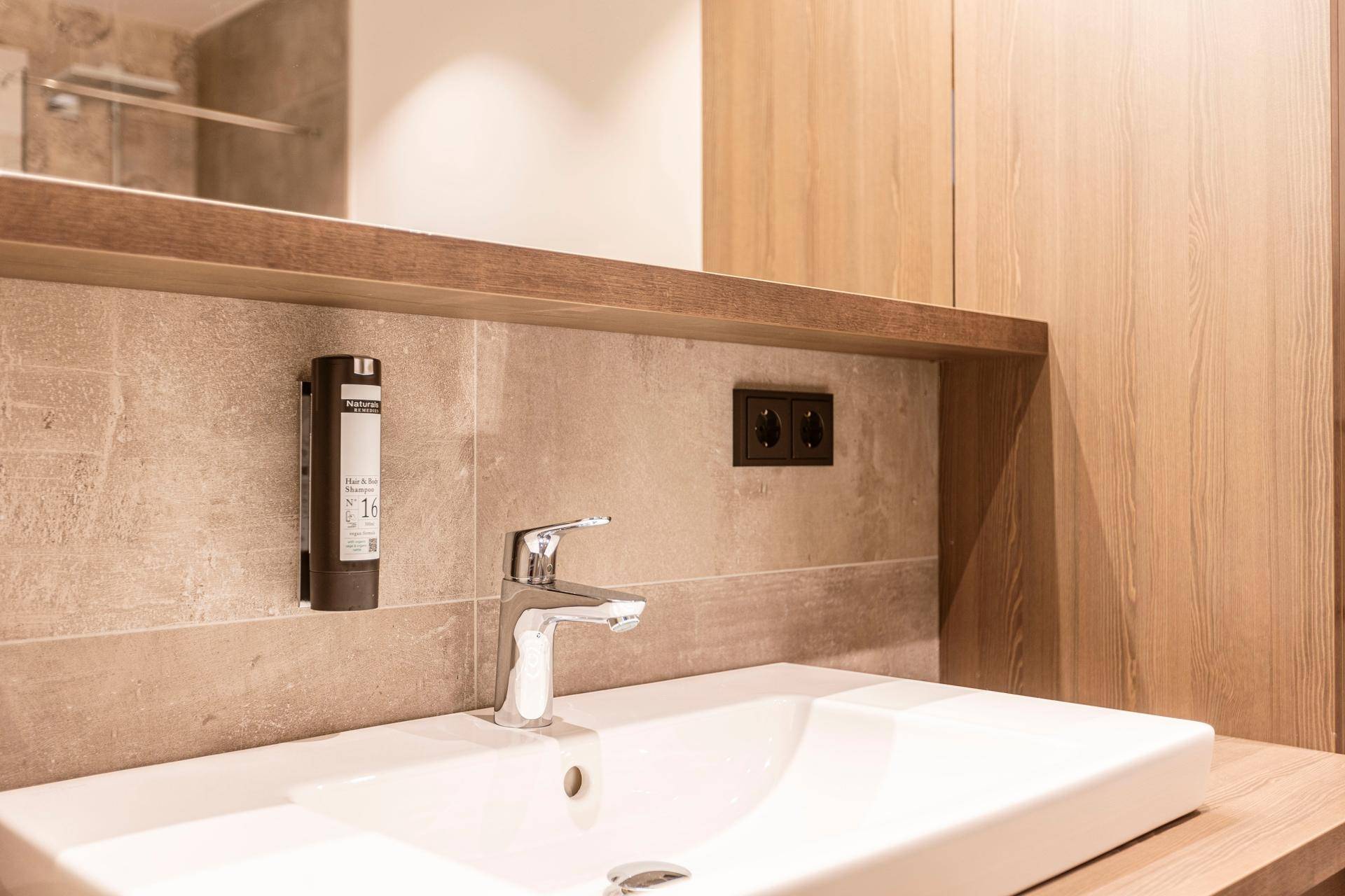Modernes Badezimmer mit elegantem Waschbecken, Armatur und Holzdetails, umgeben von hellen Fliesen.