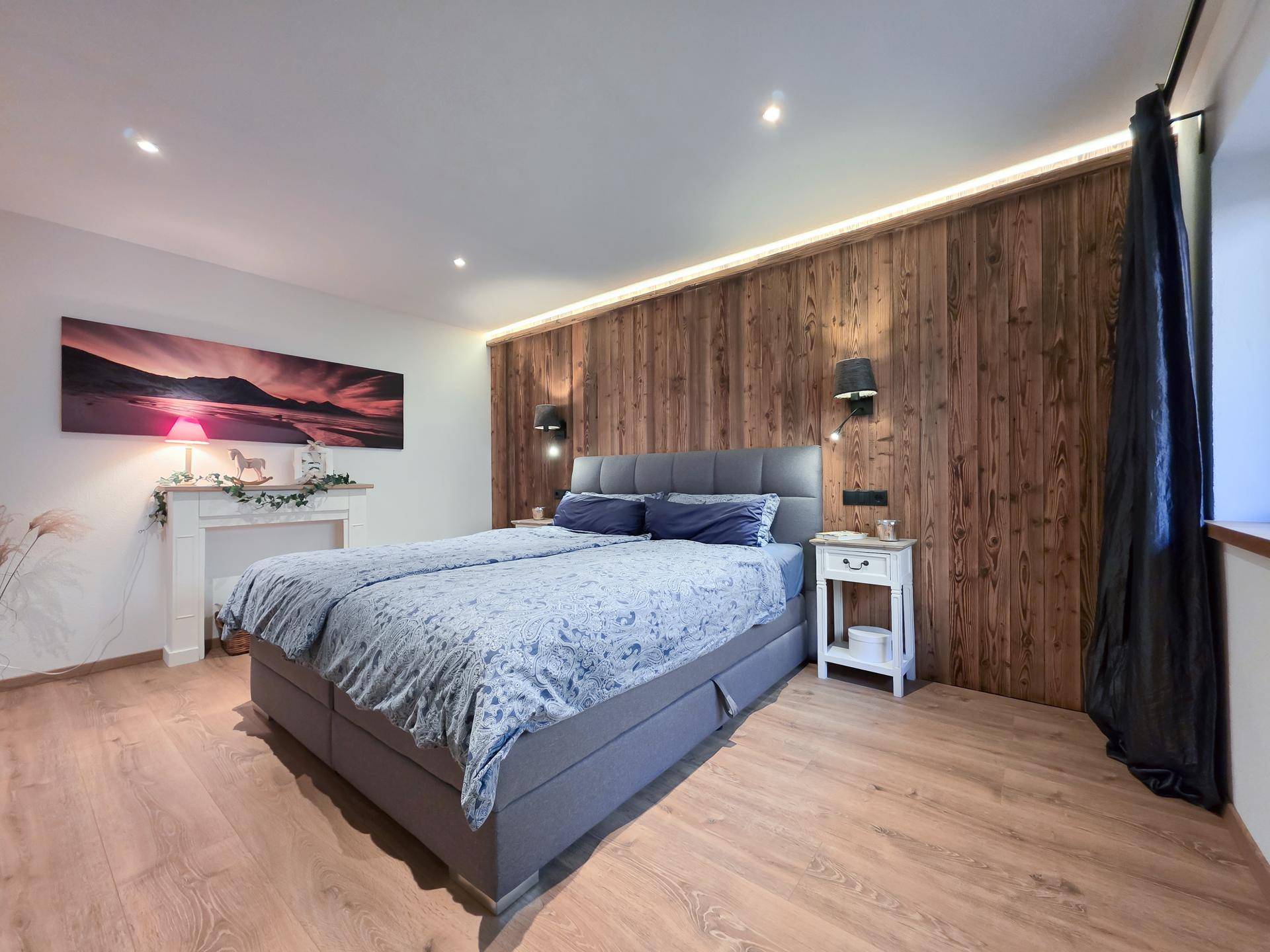 Gemütliches Schlafzimmer mit Holzwand, Doppelbett und indirekter Beleuchtung für eine warme Atmosphäre.