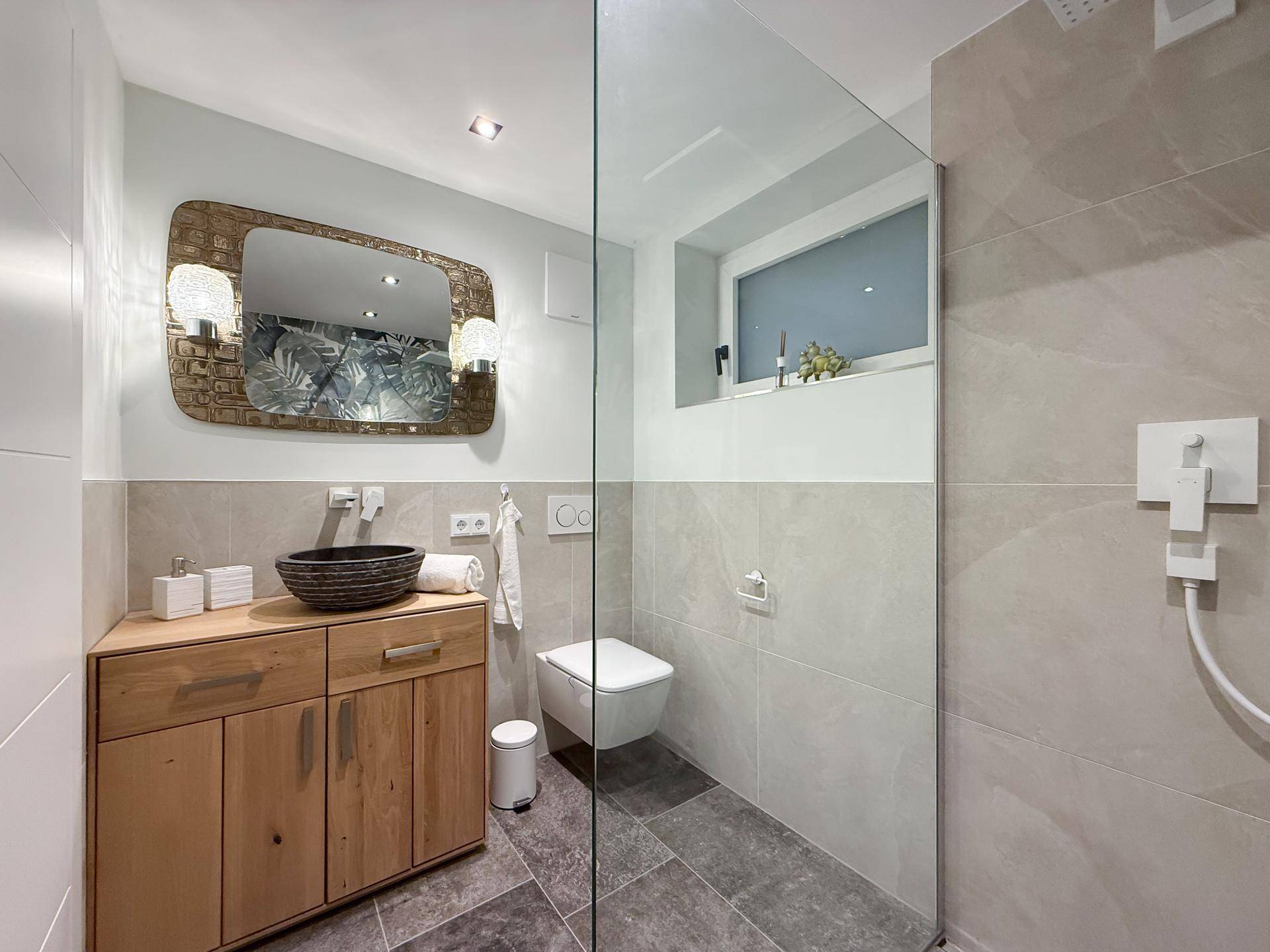 Modernes Badezimmer mit Holzwaschtisch, wandhängendem WC und begehbarer Dusche.