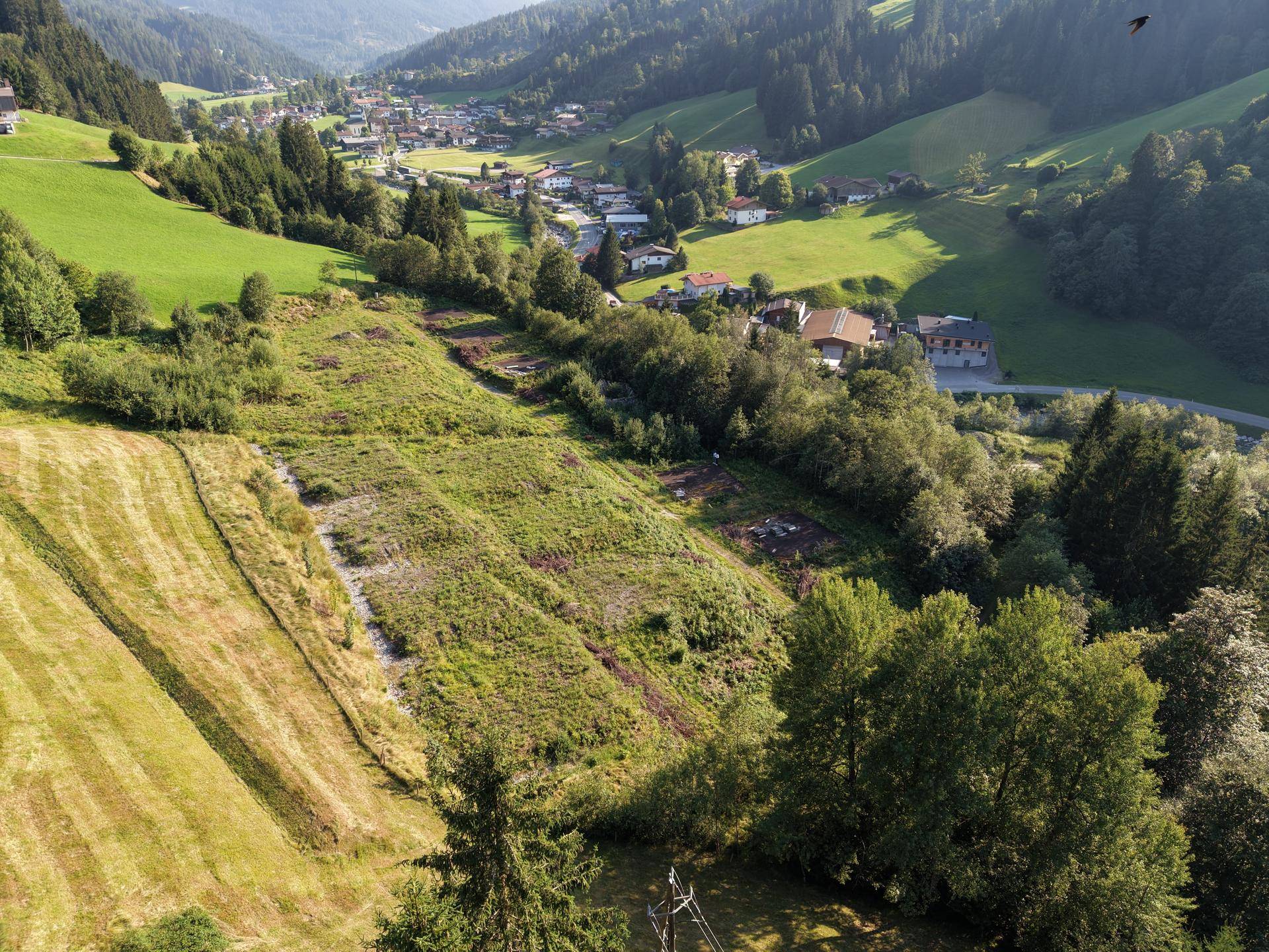 Luftaufnahme einer grünen Tallandschaft mit einem Dorf, umgeben von Wäldern und Wiesen.
