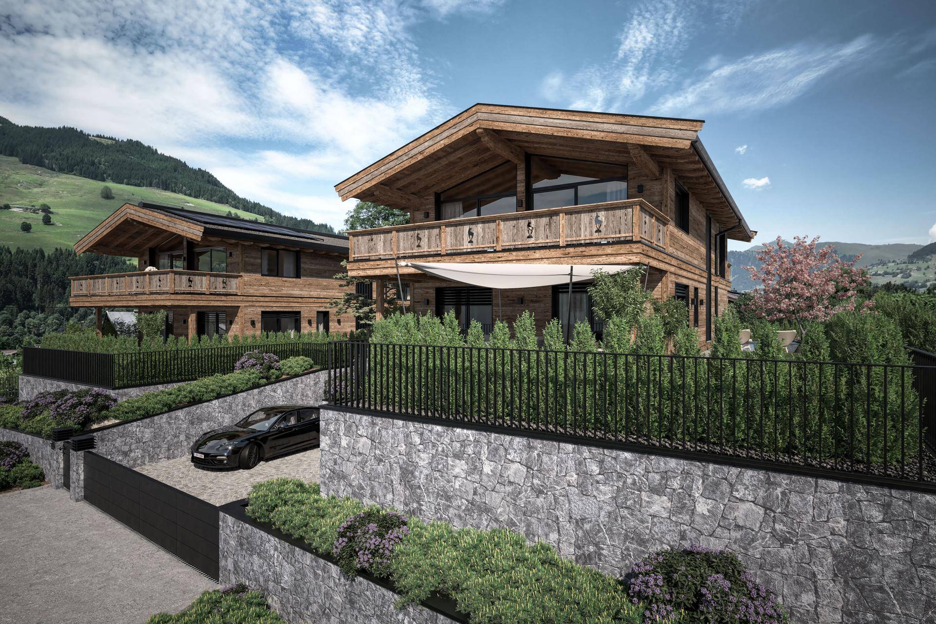 Ansicht von zwei Holzchalets mit gepflegter Hecke und Einfahrt vor einer malerischen Bergkulisse.