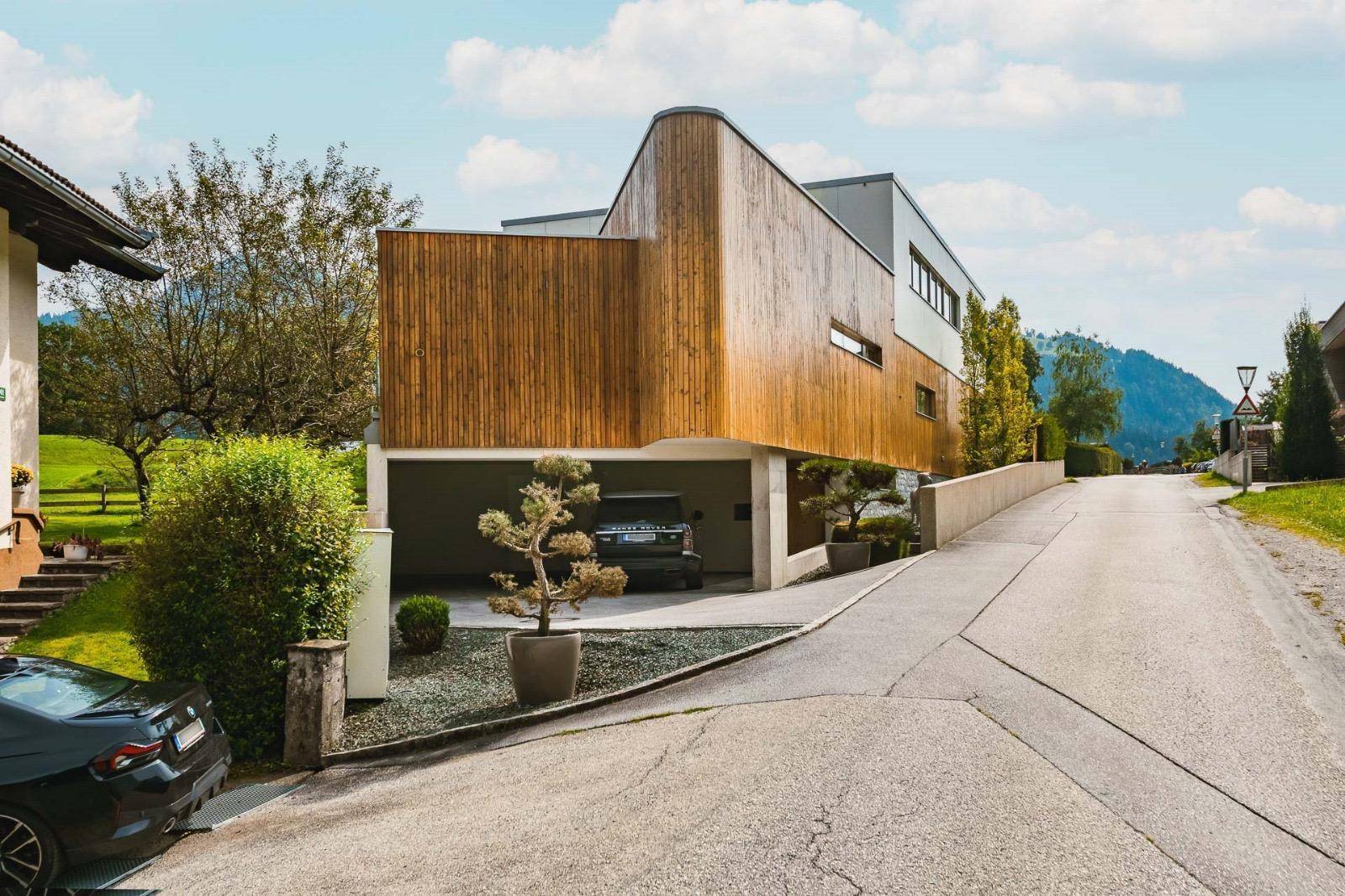 Modernes Wohnhaus mit Holzfassade und integrierter Garage, eingebettet in die ländliche Umgebung.