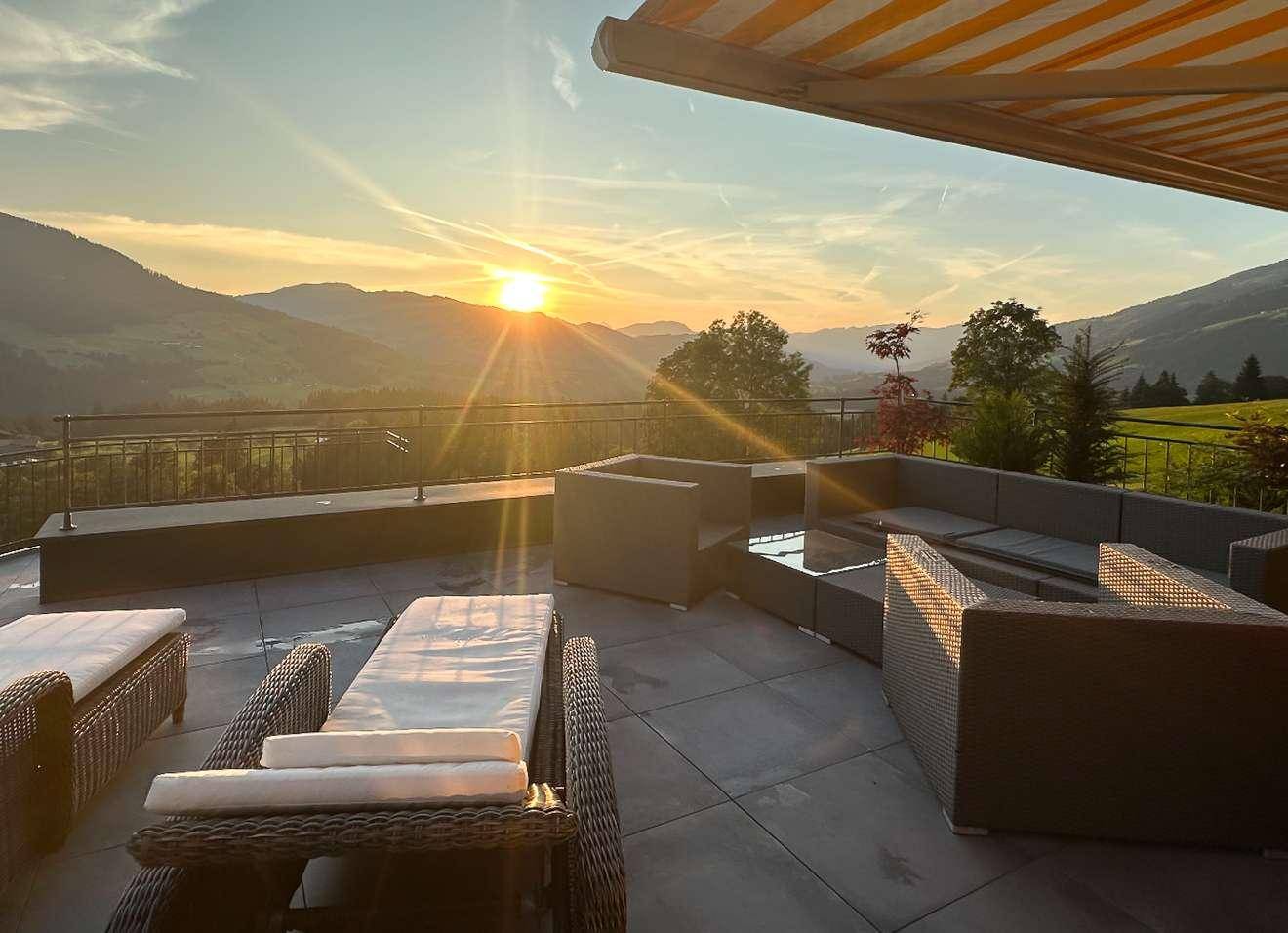 Große Sonnenterrasse mit Lounge-Möbeln und Markise, ideal für entspannte Abende mit Bergblick.