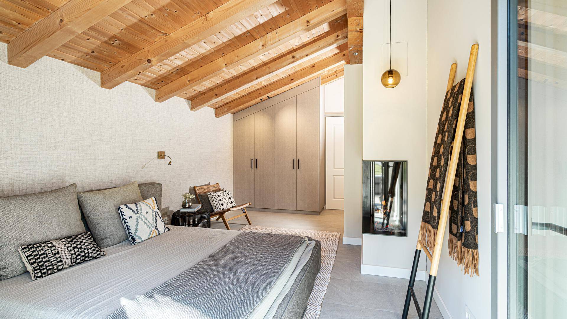 Schlafzimmer mit Holzbalkendecke, Einbauschränken und modernem Kamin.