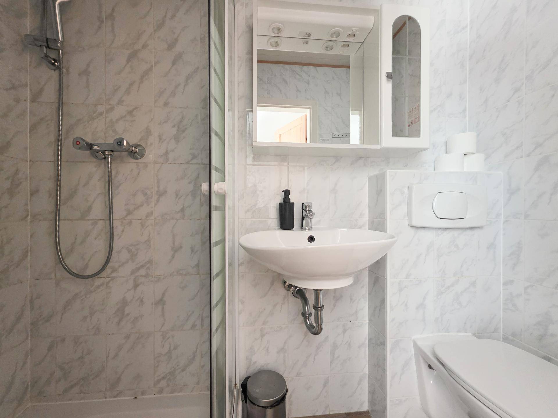 Funktionales Badezimmer mit Dusche, Waschbecken, WC und hellen Fliesen.