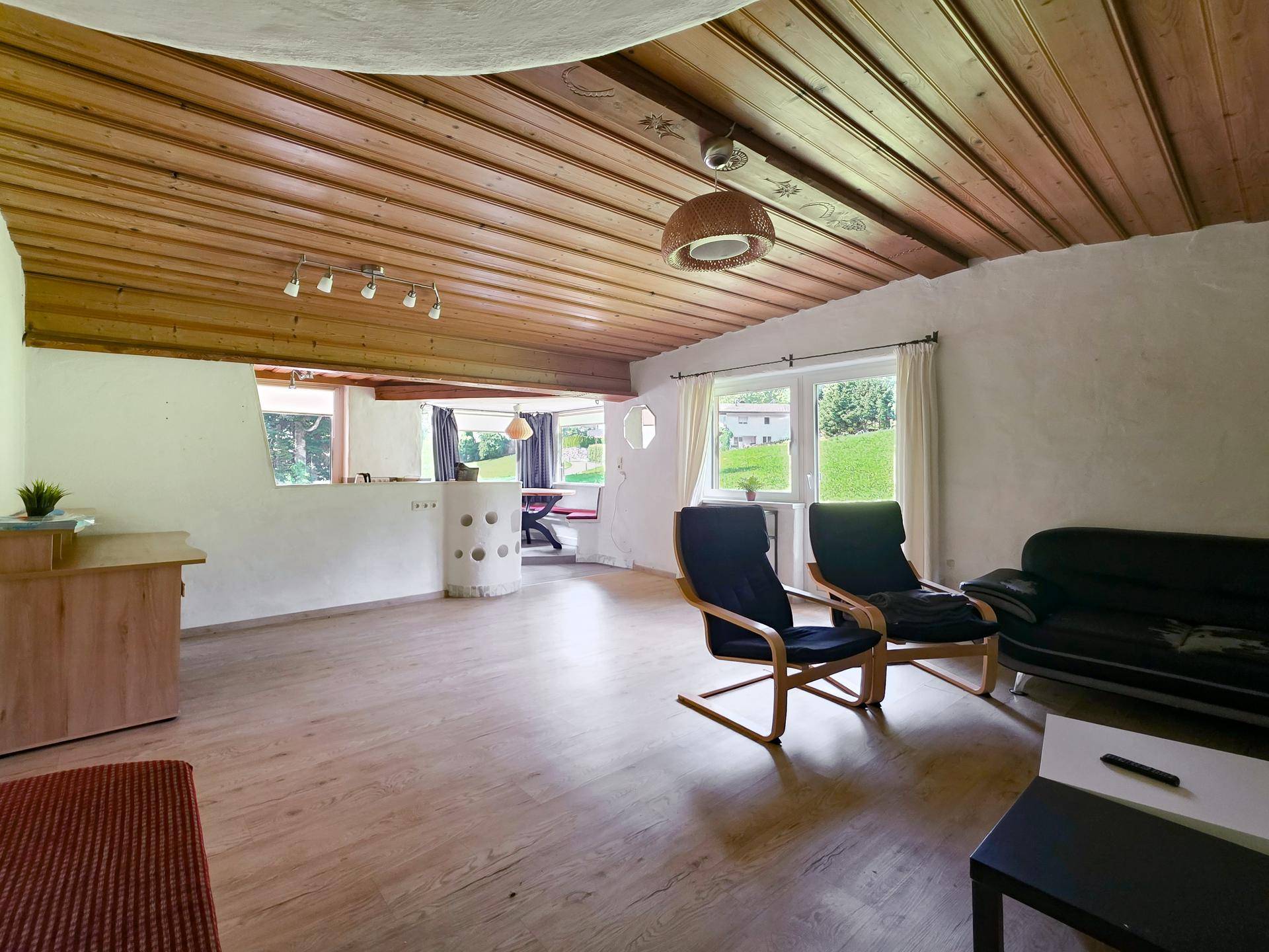 Gemütliches Wohnzimmer mit Holzbalkendecke, hellem Laminatboden und Blick ins Grüne.