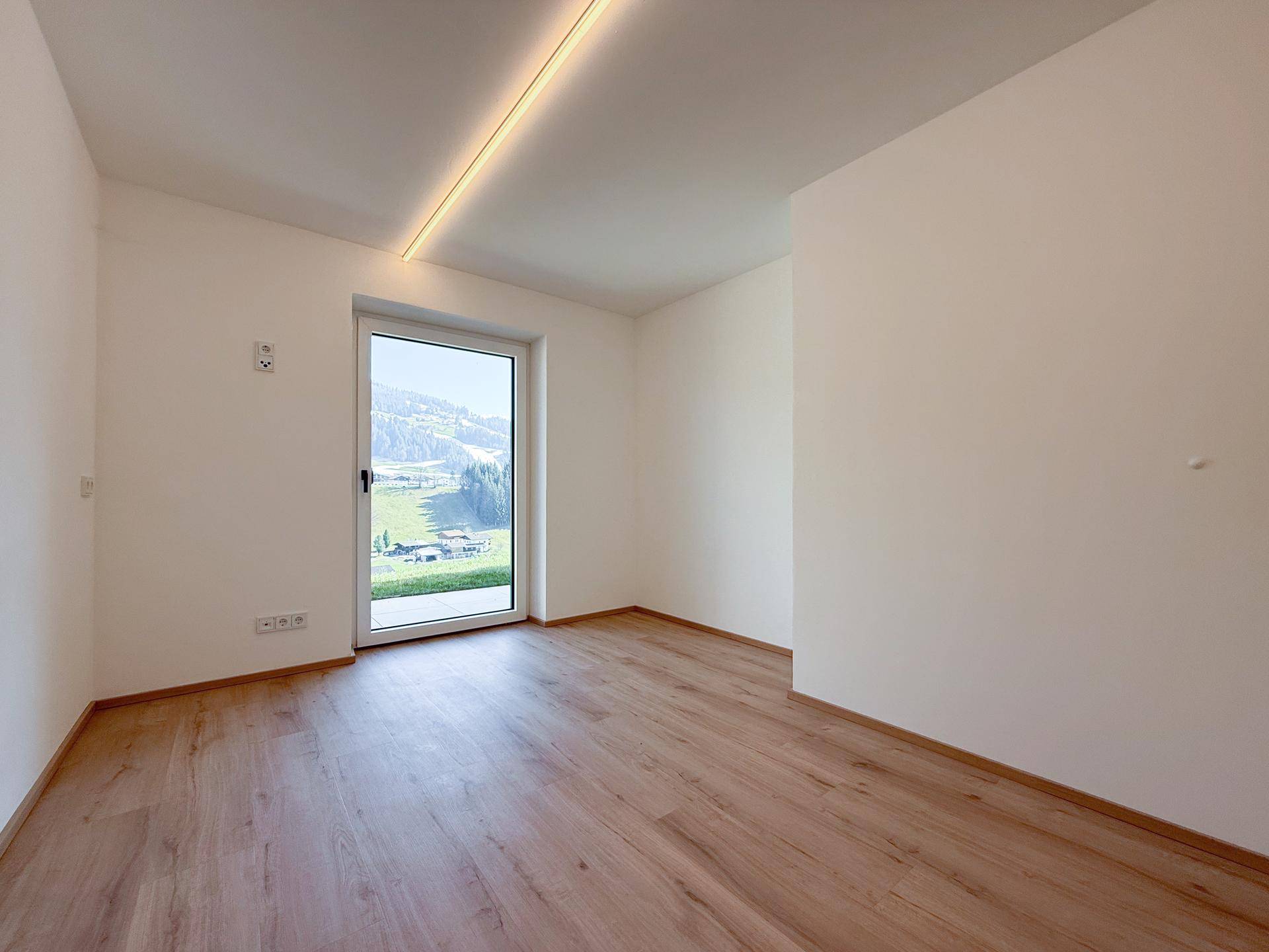 Heller, leerer Raum mit Holzboden und Fenster mit Zugang nach draußen.