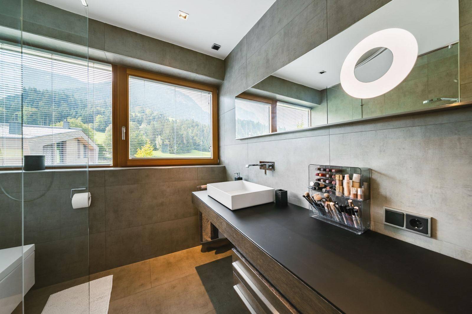Modernes Badezimmer mit großem Waschtisch, Spiegel und Blick auf die grüne Landschaft.