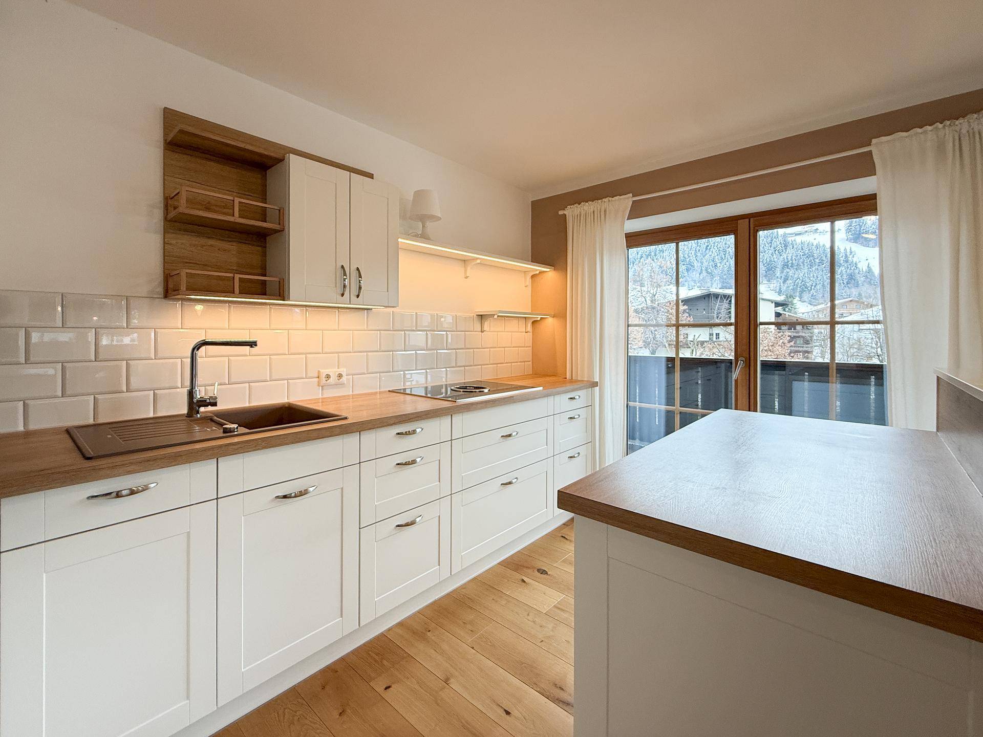 Helle Küche mit weißen Schränken, Holzarbeitsplatten und Zugang zum Balkon mit Bergblick.