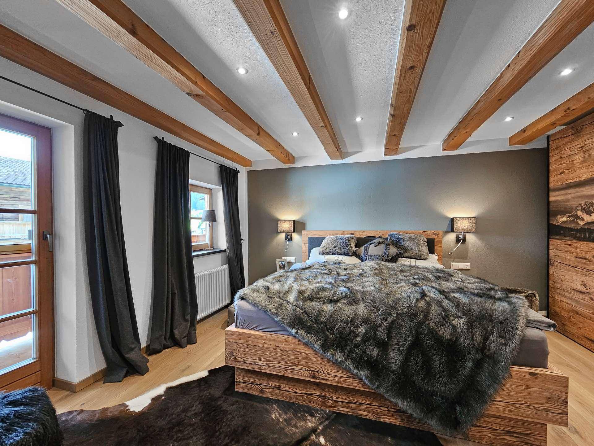 Schlafzimmer mit rustikalem Holzbett, Holzbalkendecke und direktem Zugang zu einem kleinen Balkon.