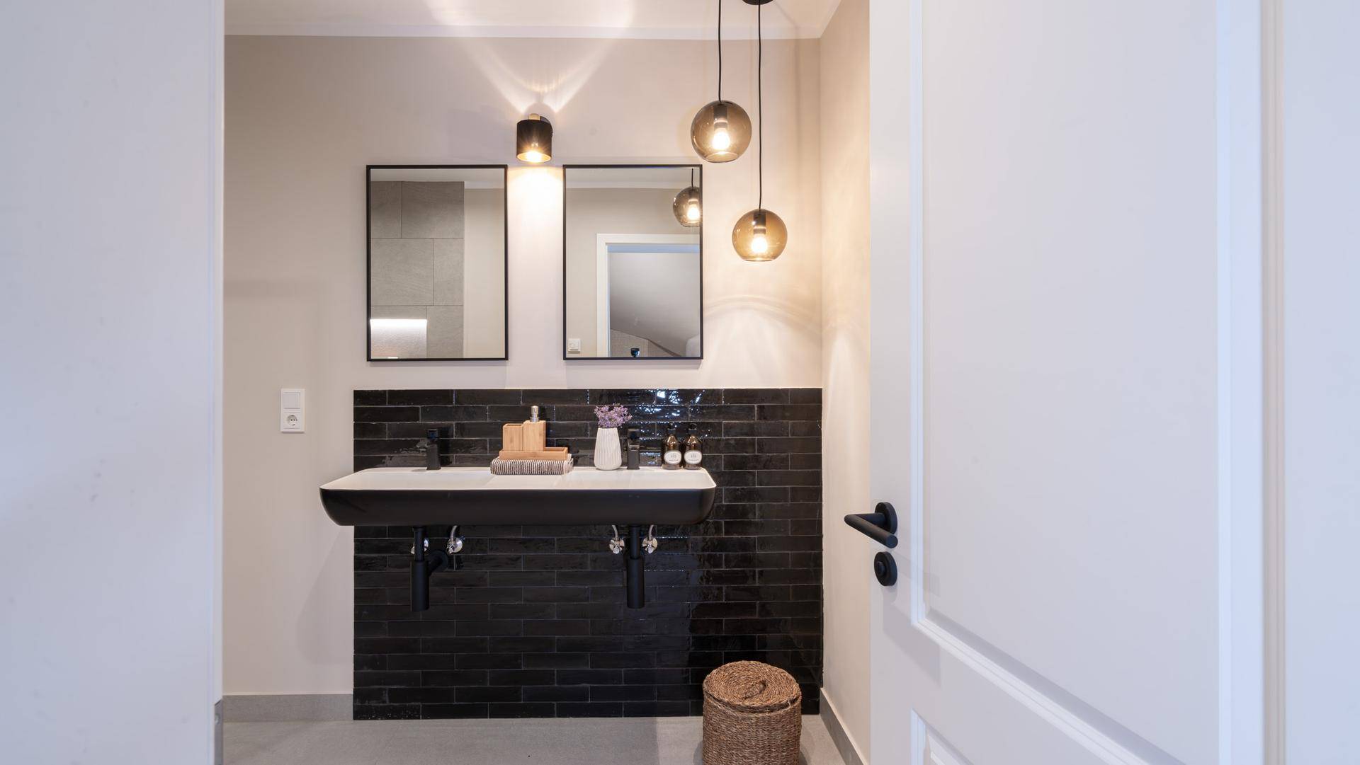 Modernes Badezimmer mit Doppelwaschbecken, schwarzen Armaturen und stilvollen Hängelampen.