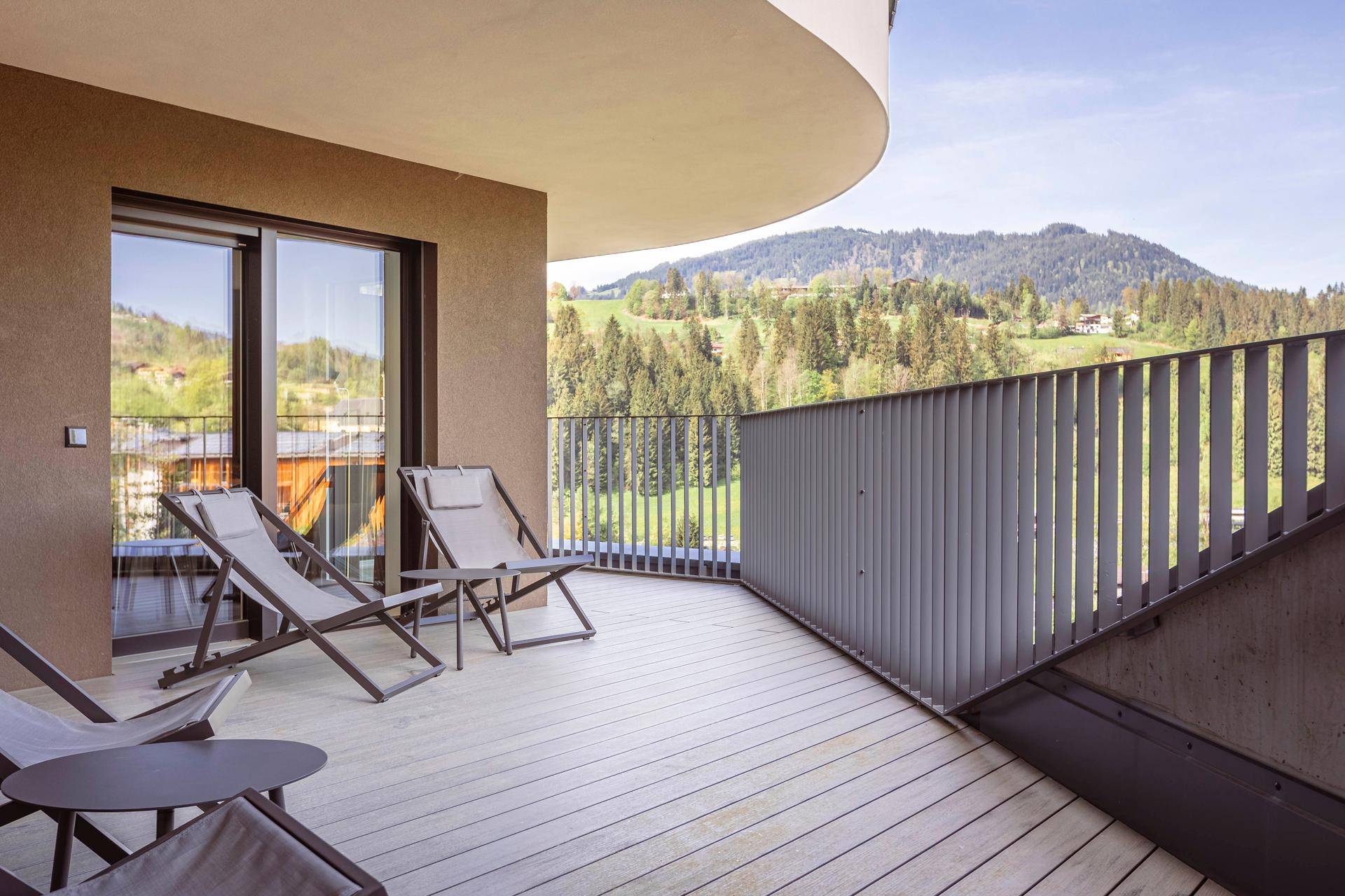 Geräumiger, geschwungener Balkon mit Holzdeck und bequemen Liegestühlen, bietet einen weiten Bergblick.