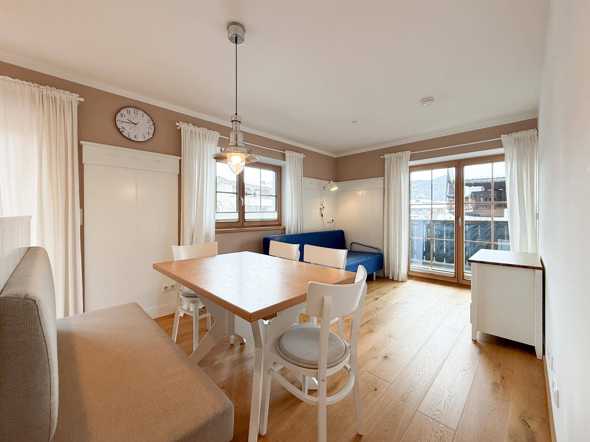 Gemütlicher Wohn-Essbereich mit Holzboden, Esstisch und Zugang zu einem Balkon.