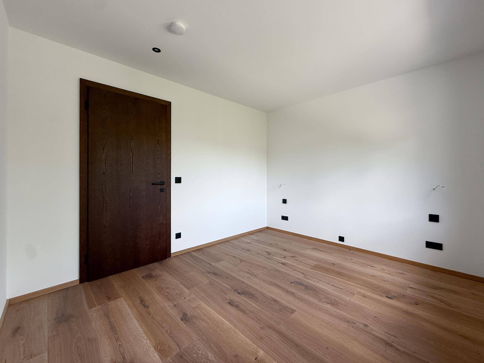 Helles, leeres Zimmer mit Holzboden und dunkler Holztür, bereit zur individuellen Gestaltung.
