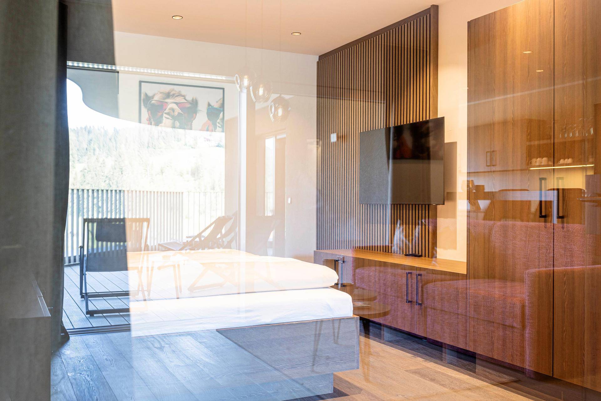 Schlafzimmer mit Doppelbett, reflektiert in der Glasfront zum Balkon mit Bergblick.