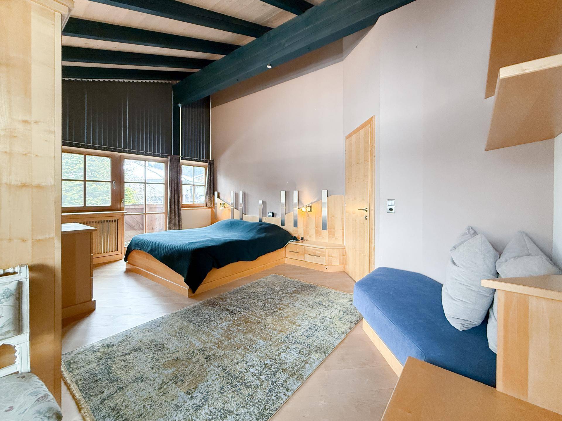 Helles Schlafzimmer mit Holzbalkendecke, Doppelbett und Fenster mit Blick ins Grüne.