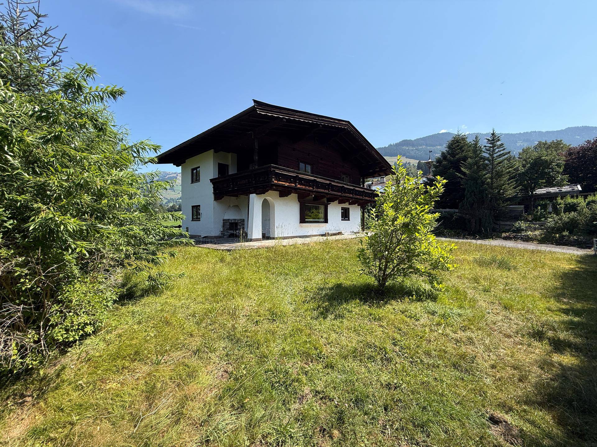 Seitenansicht des Hauses mit weißer Fassade und Holzbalkon, umgeben von einer grünen Wiese.