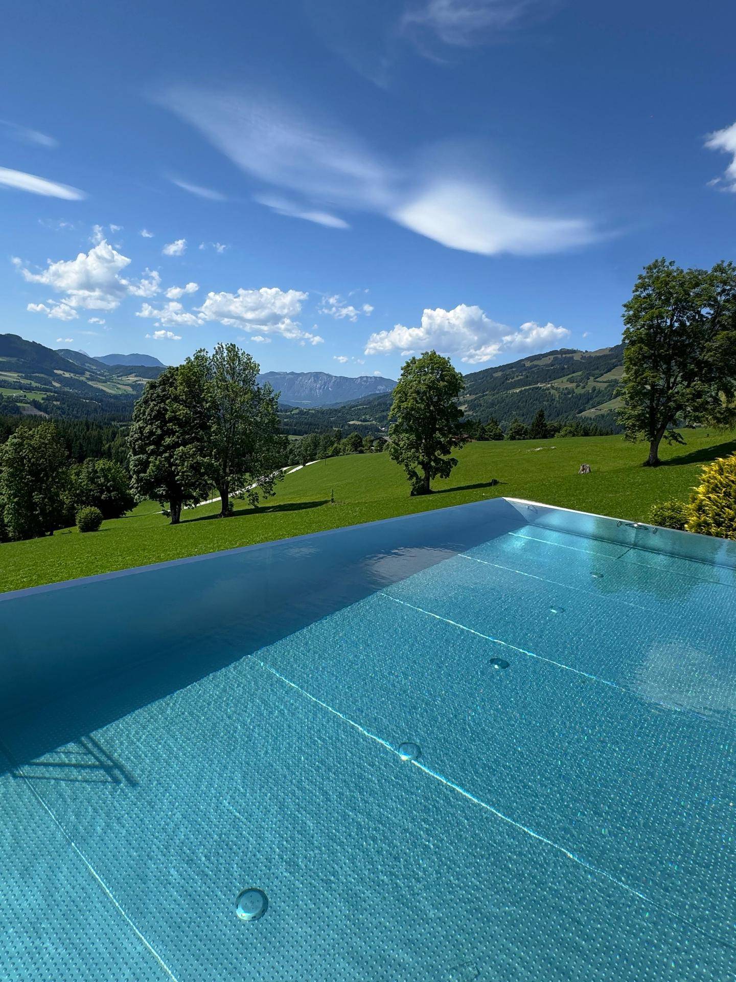 Infinity-Pool mit kristallklarem Wasser und weitem Blick auf die grüne Berglandschaft.