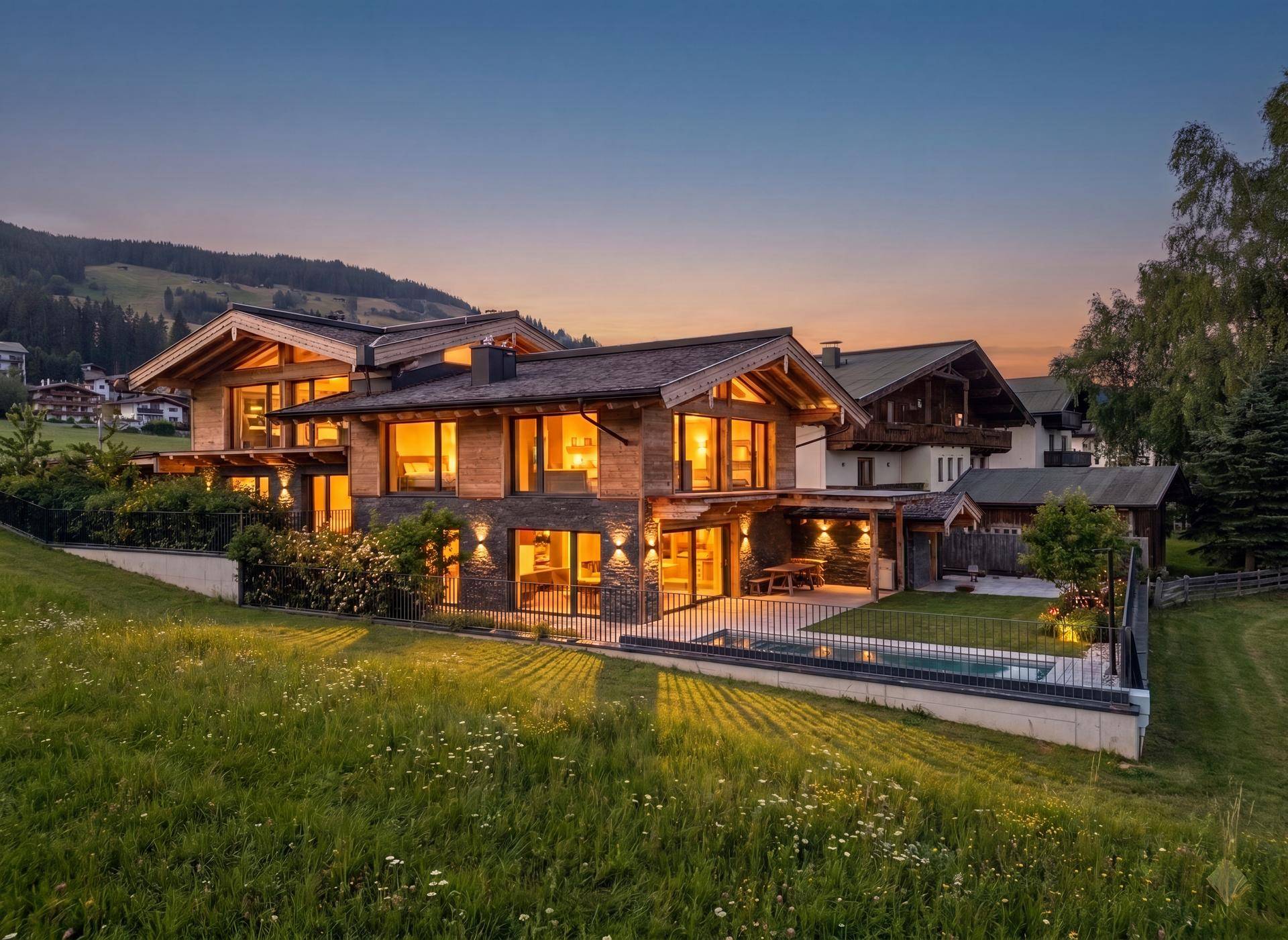 Abendliche Ansicht des Chalet-Hauses mit beleuchteter Terrasse, Pool und Bergblick.