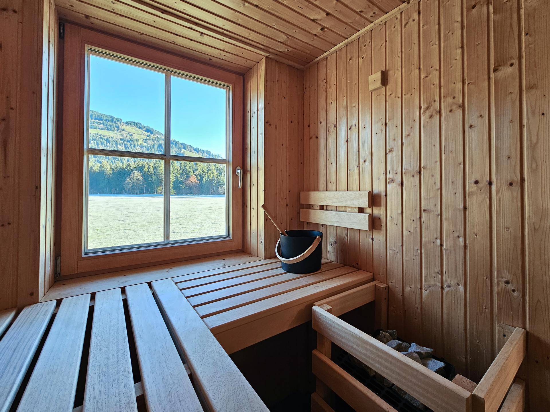 Gemütliche Holzsauna mit Blick durch das Fenster auf die winterliche Natur und die umliegenden Berge.