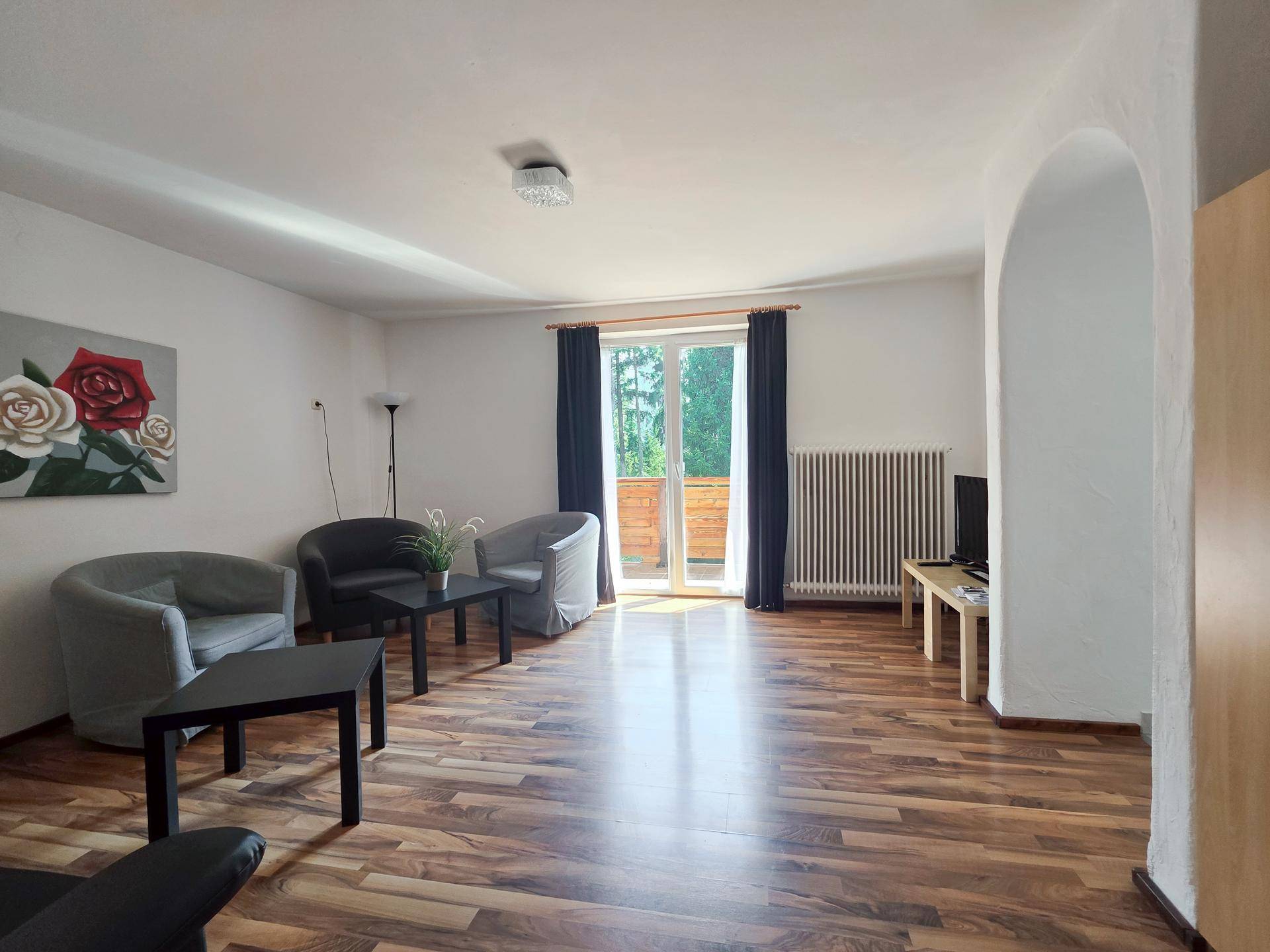 Geräumiges Wohnzimmer mit dunklem Laminatboden, bequemen Sitzmöbeln und Zugang zum Balkon.