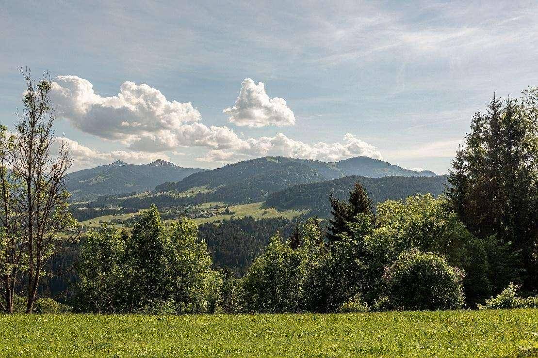 Weitläufiger Blick über grüne Hügel und bewaldete Berge unter einem bewölkten Himmel.