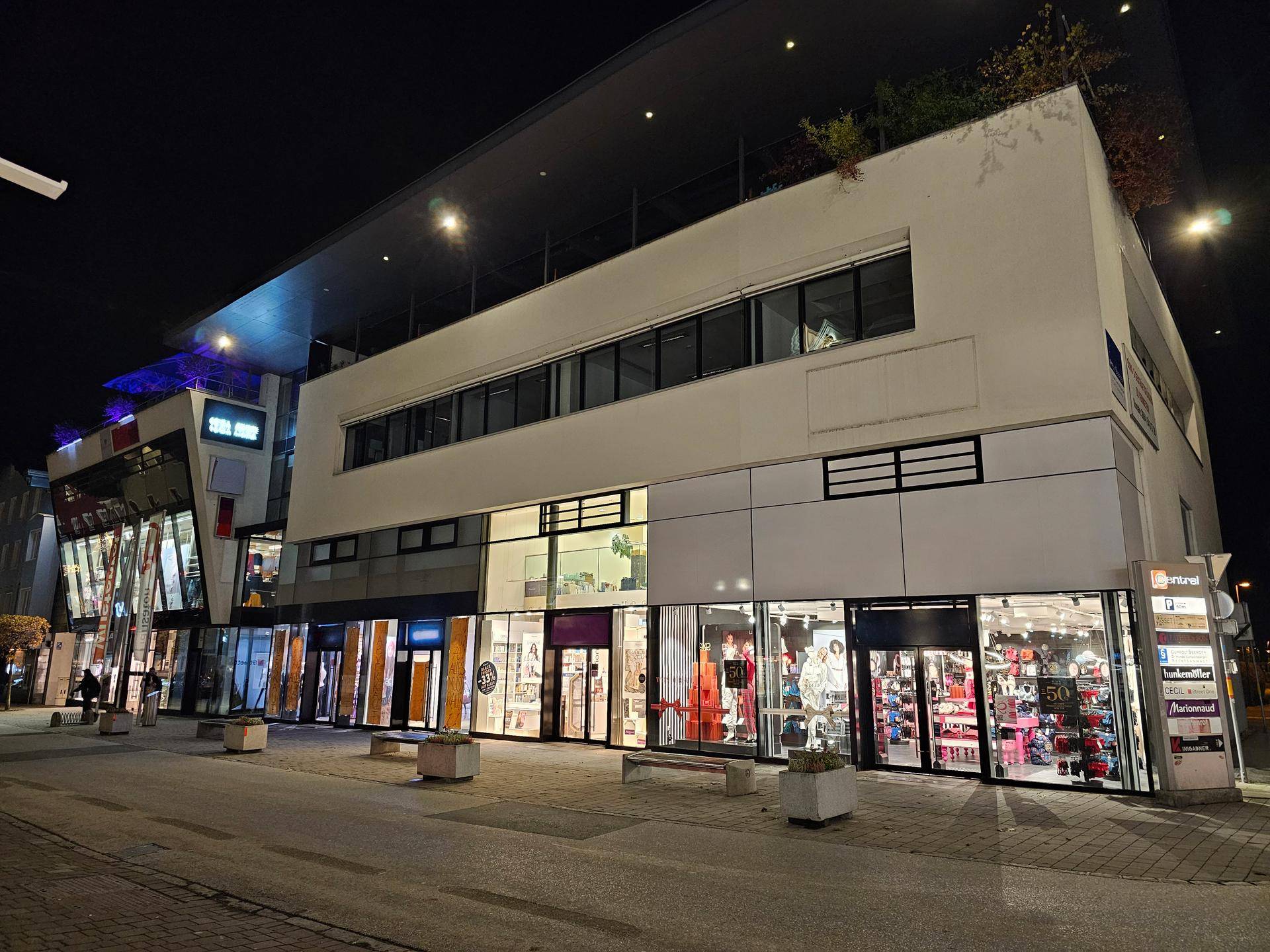 Ansicht der modernen Geschäftsfassade bei Nacht mit verschiedenen beleuchteten Ladenfronten und einem klaren Himmel.