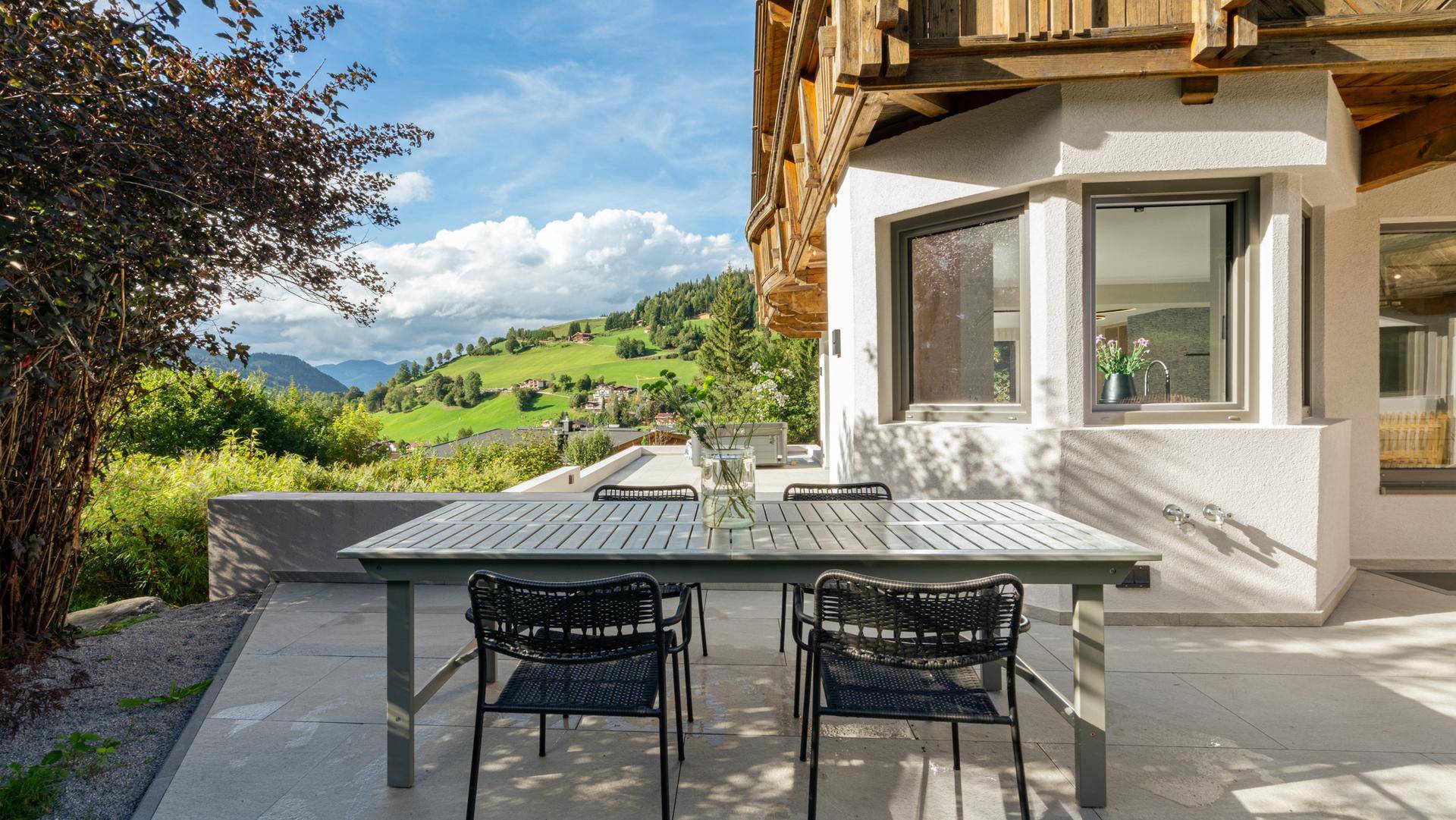 Sonnenterrasse mit modernem Esstisch und weitem Blick über die grüne Landschaft und die Berge.
