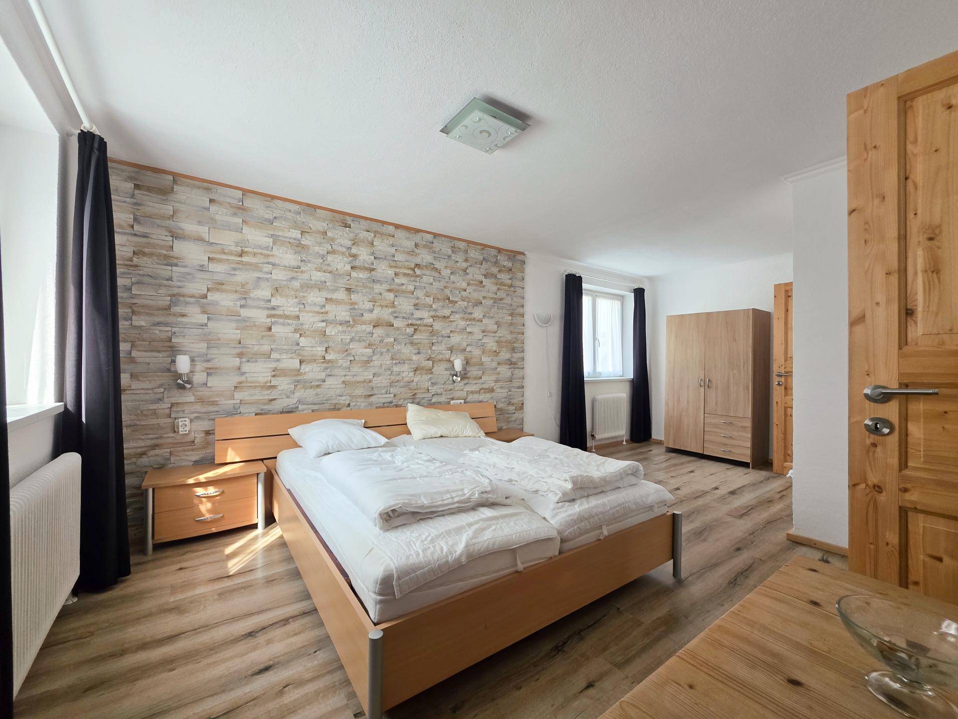 Schlafzimmer mit Doppelbett, dekorativer Steinwand und hellem Laminatboden.