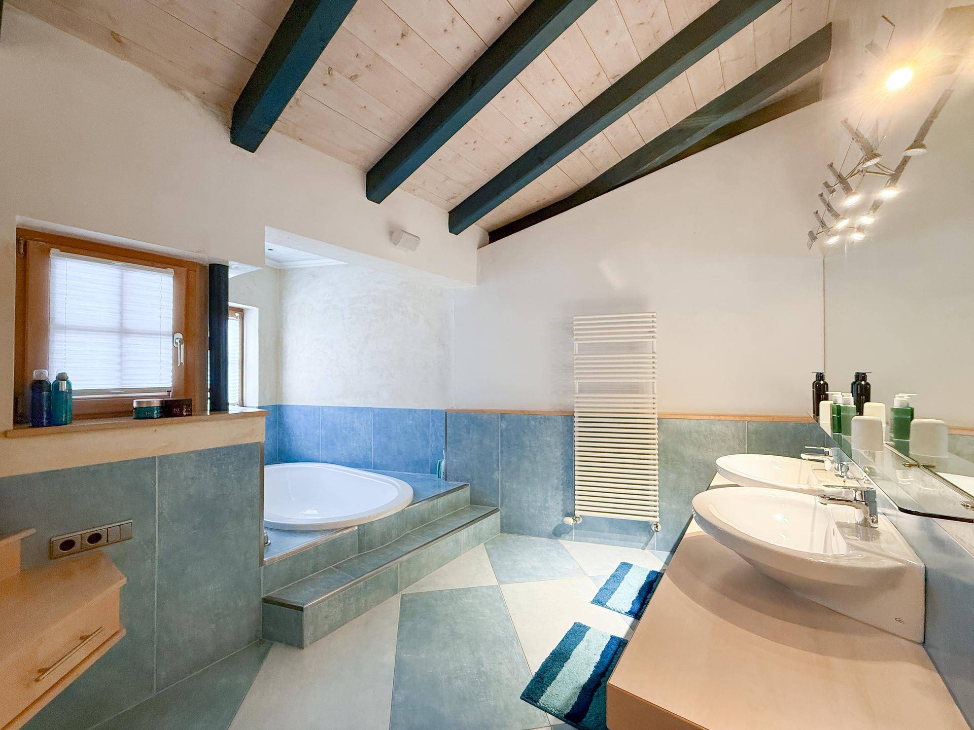 Helles Badezimmer mit Badewanne, Doppelwaschbecken und beheiztem Handtuchhalter.