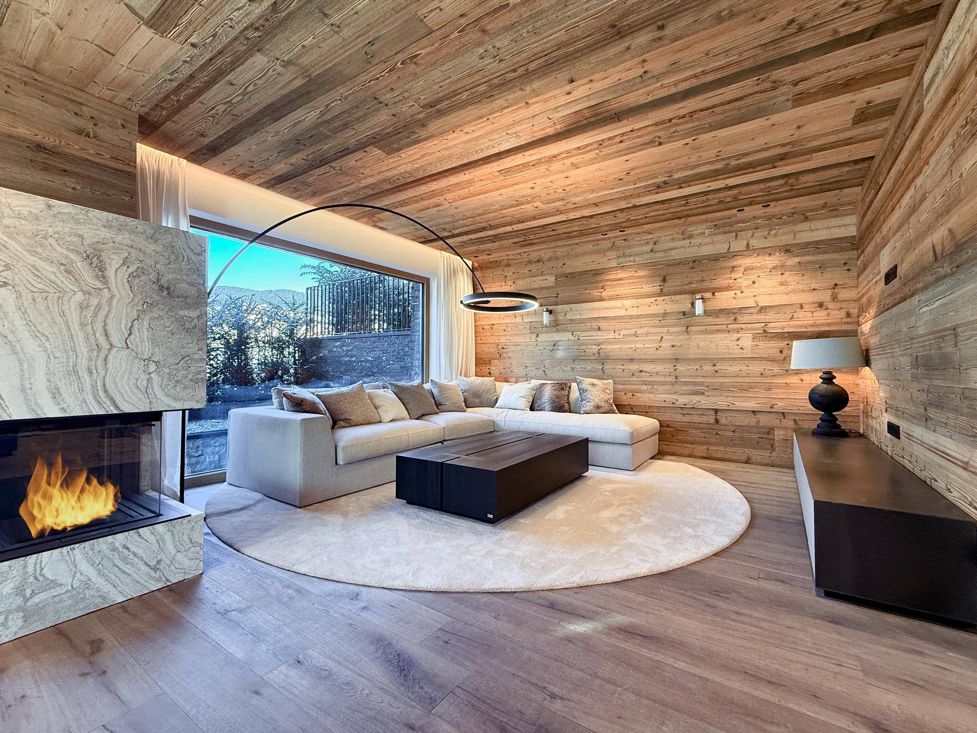 Gemütliches Wohnzimmer mit Holzwänden, modernem Kamin und großem Fenster mit Bergblick.