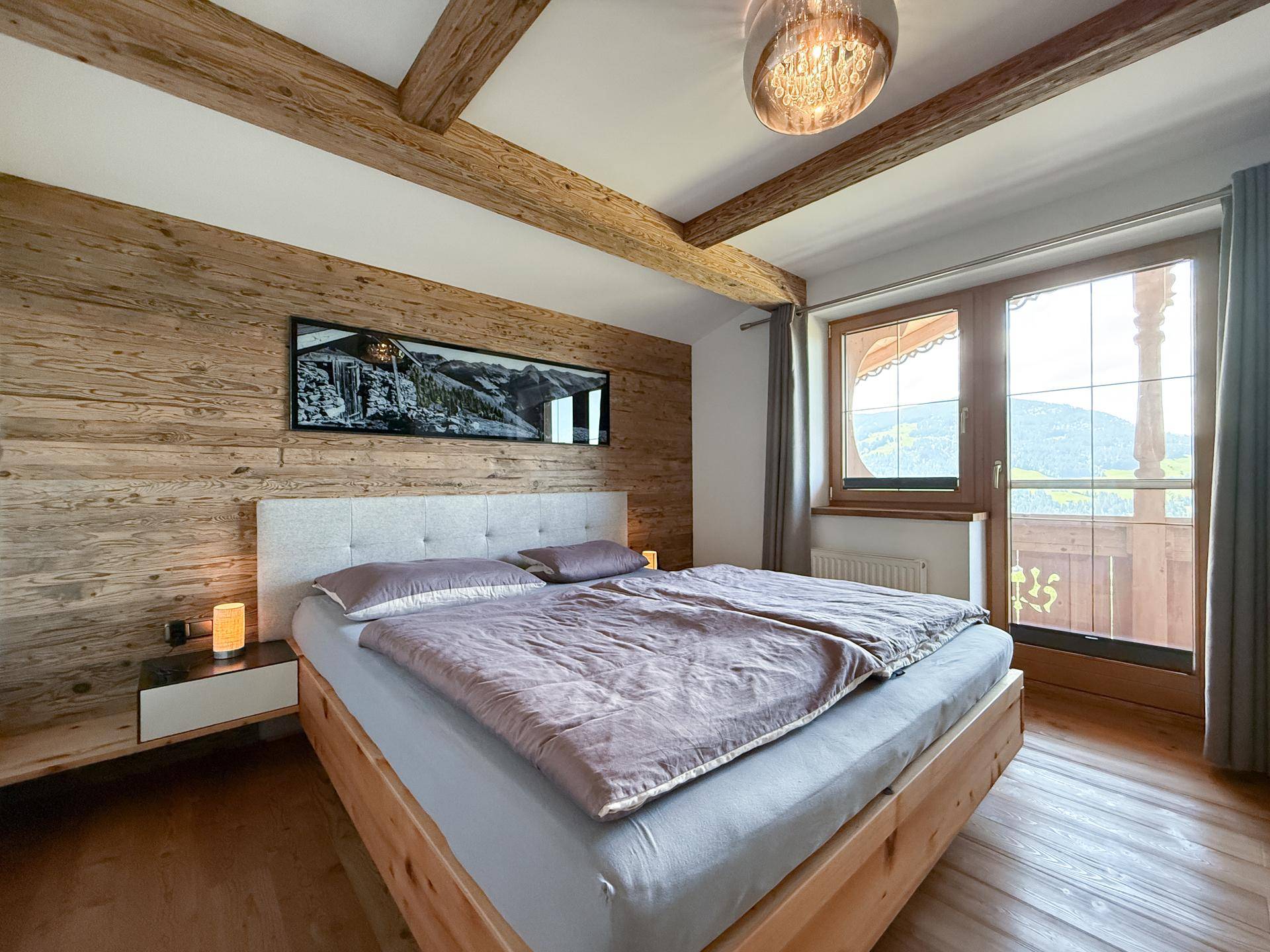 Gemütliches Schlafzimmer mit Holzwänden, Doppelbett und Zugang zum Balkon.