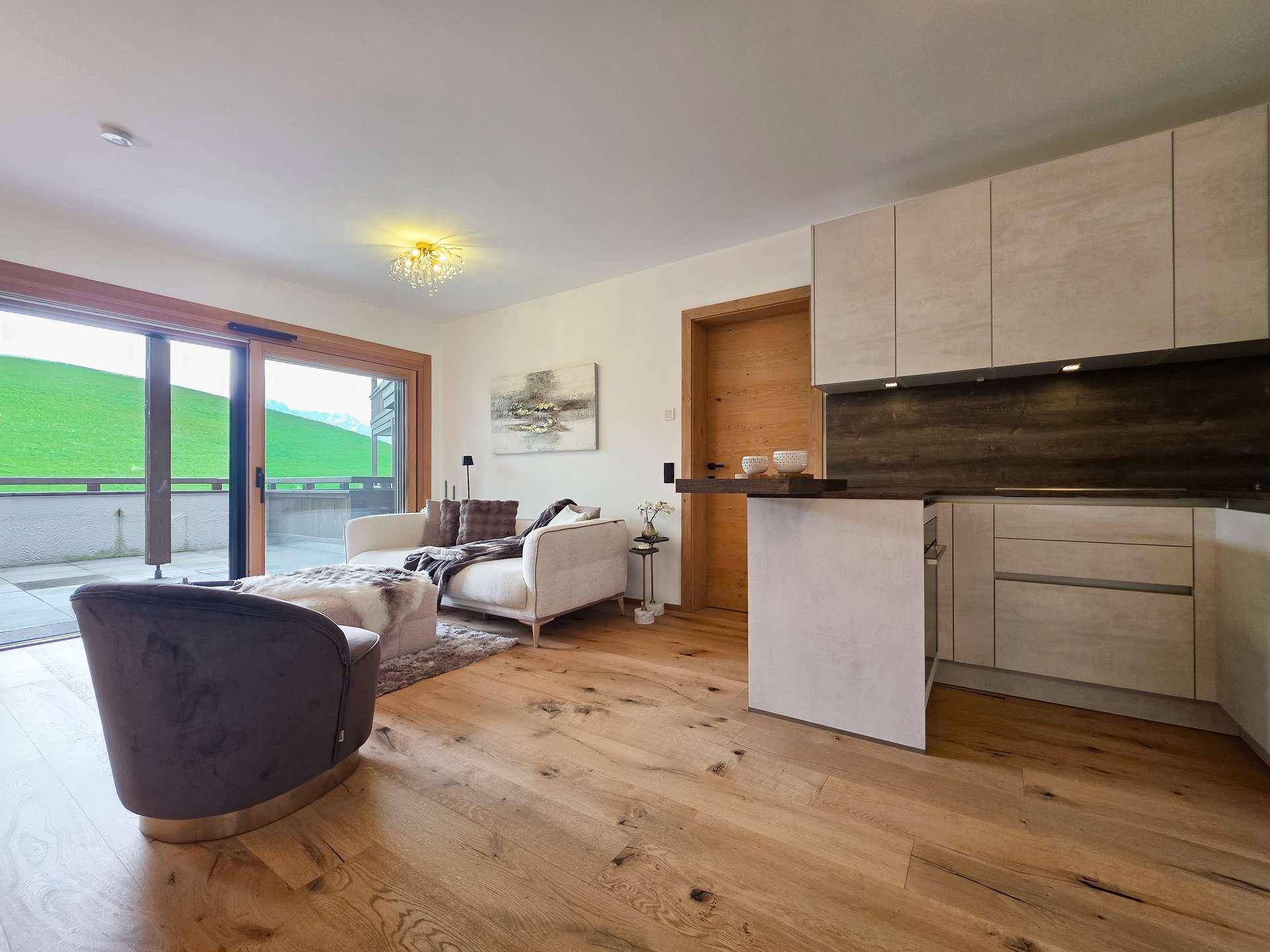Moderner Wohnbereich mit Holzboden und integrierter Küchenzeile, mit Zugang zur Terrasse.