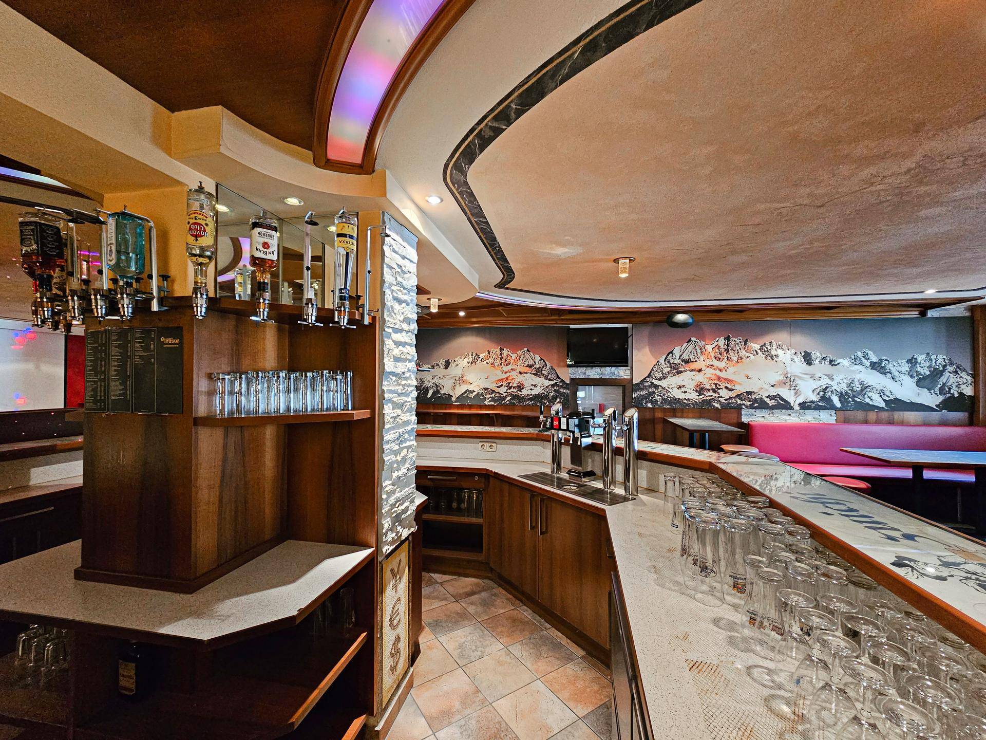 Detailansicht der Bar mit Zapfanlage, Gläsern und einer Wanddekoration mit Bergmotiv.