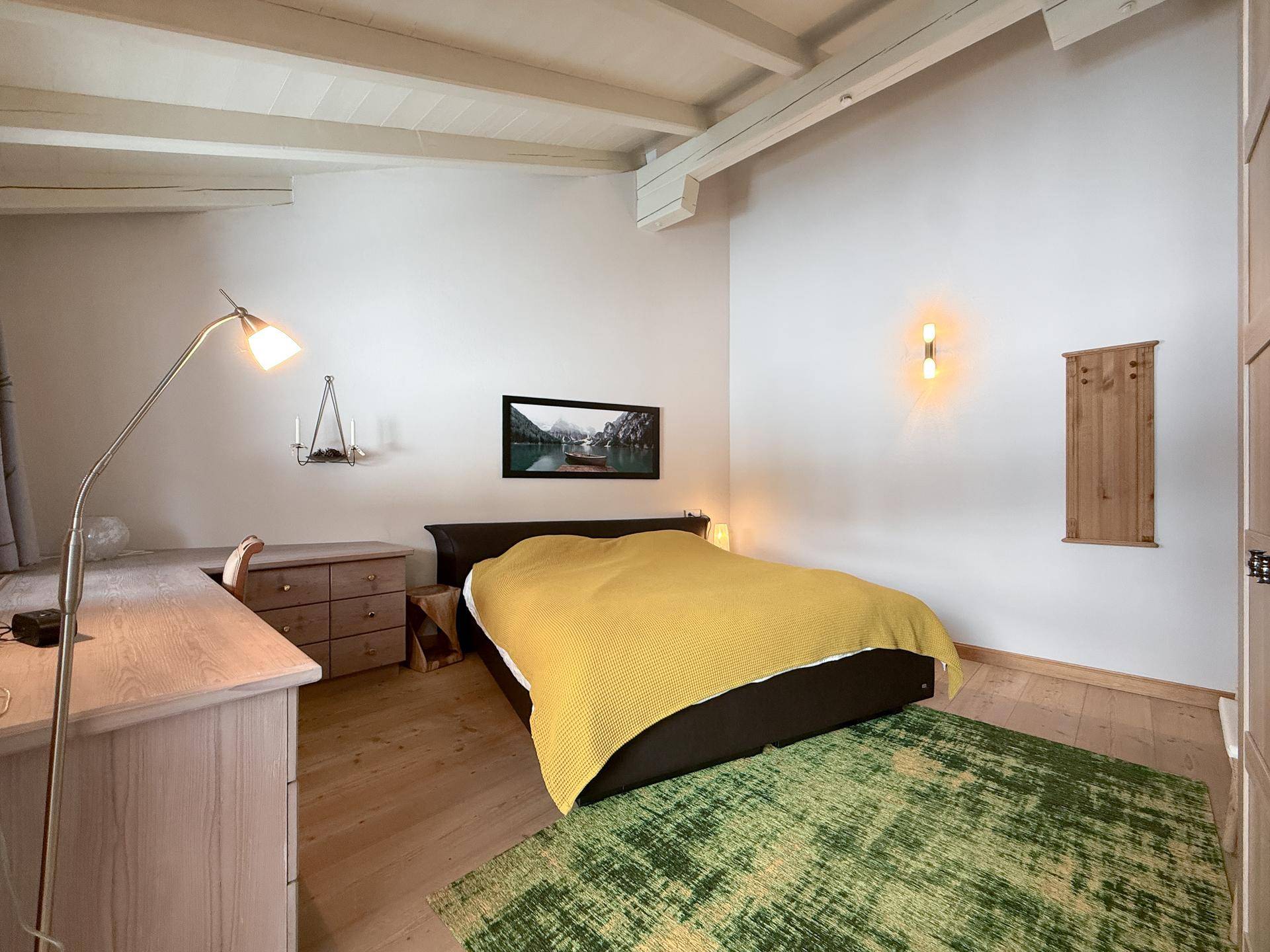 Gemütliches Schlafzimmer mit Holzbalkendecke, gelber Bettdecke und Holzboden.