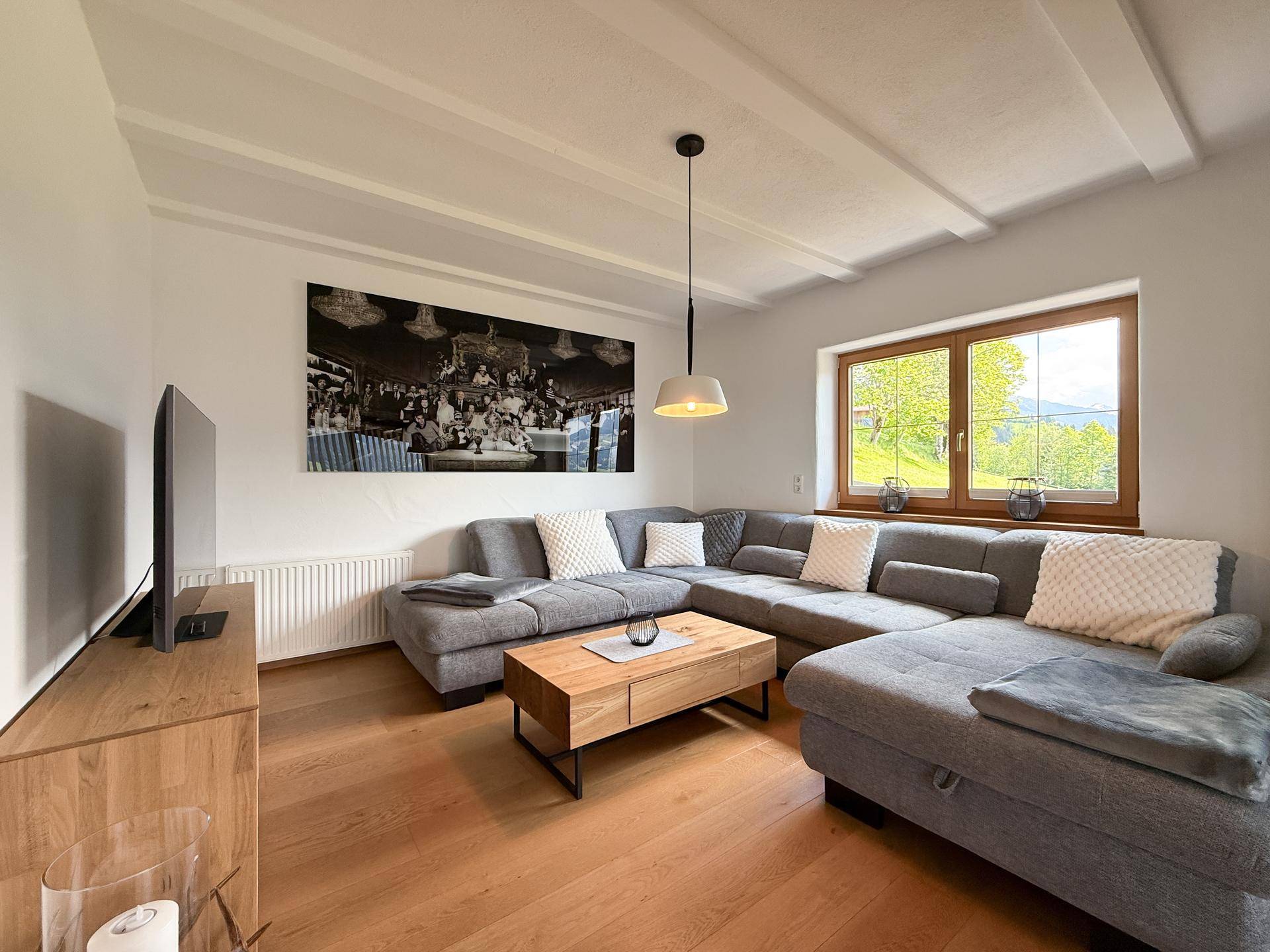 Helles Wohnzimmer mit großem Ecksofa, Holzboden und Blick ins Grüne.