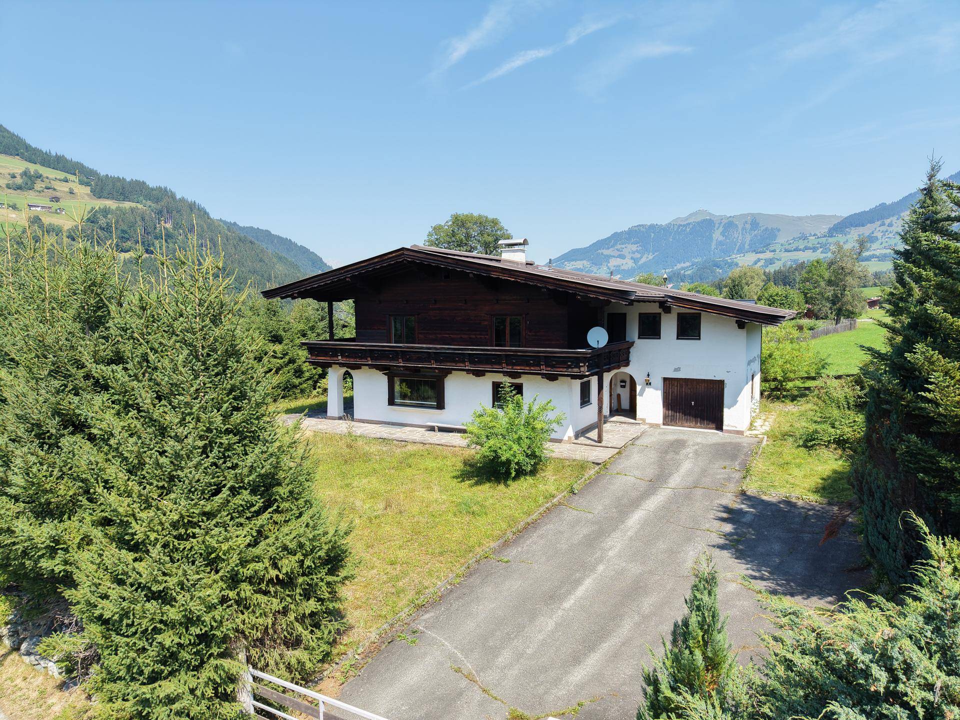 Frontansicht des Hauses mit Garage und Zufahrt, umgeben von alpiner Natur und Bäumen.