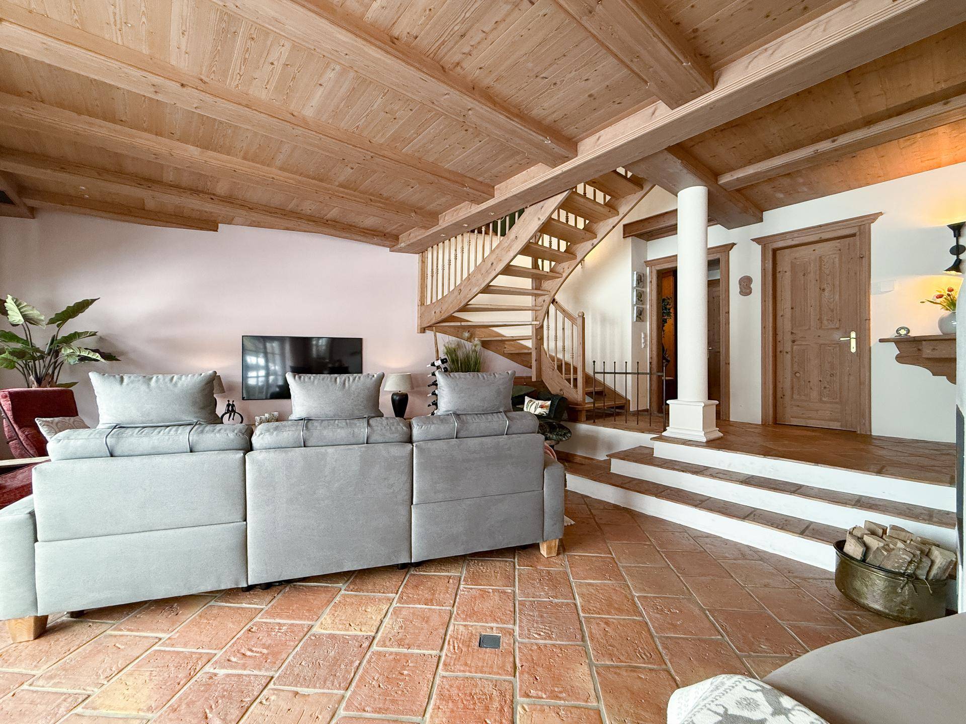 Wohnzimmer mit Holzbalkendecke, farbigen Fliesenboden und einer eleganten Holztreppe.