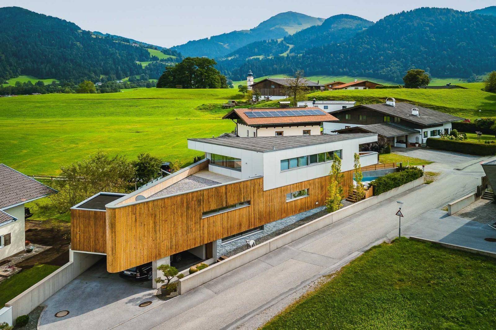 Luftaufnahme des modernen Hauses mit Holzfassade, Pool und umliegender grüner Landschaft.