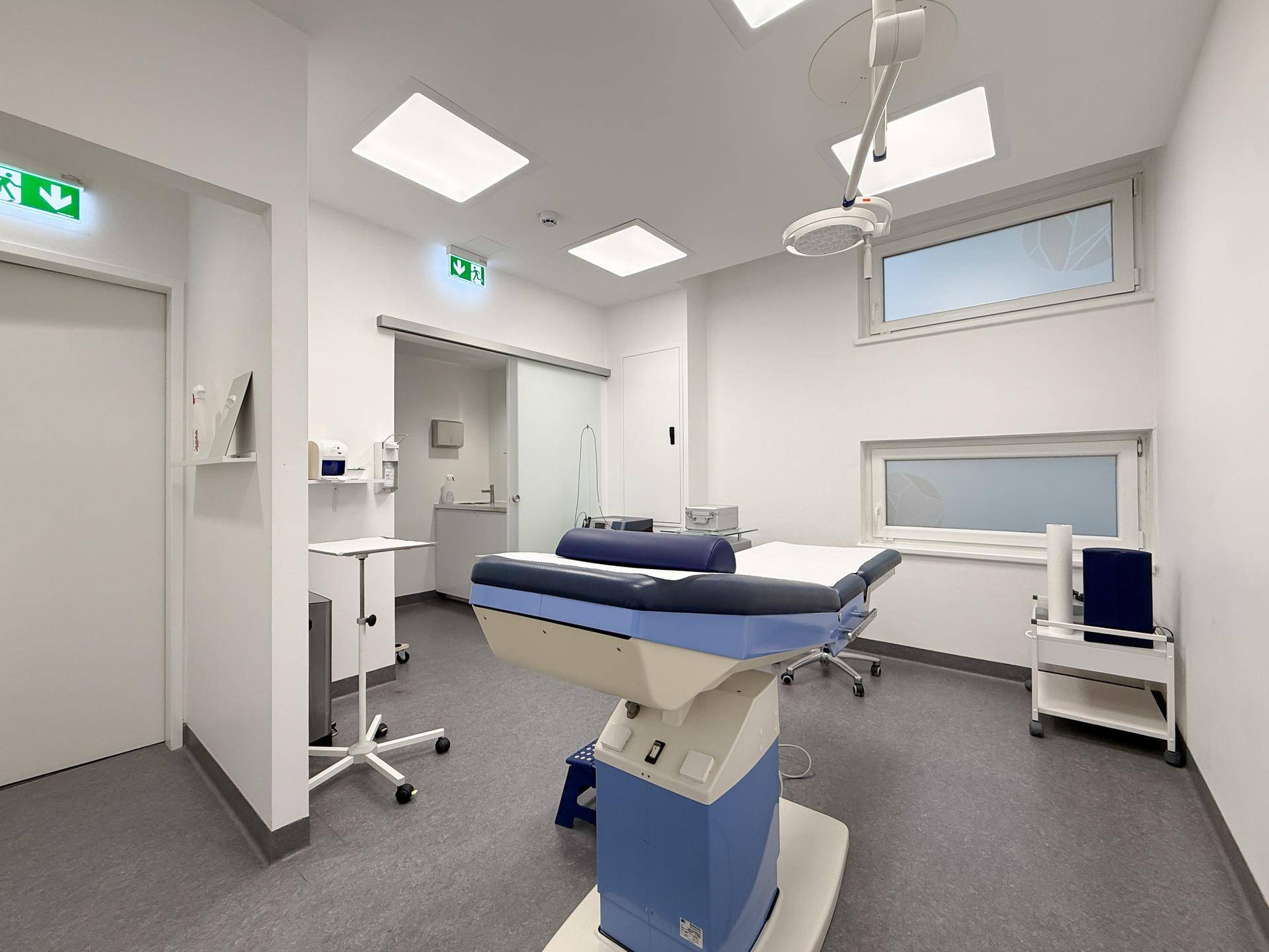 Spezialisierter Behandlungsraum mit fortschrittlicher medizinischer Liege, Waschbereich und Fenstern.