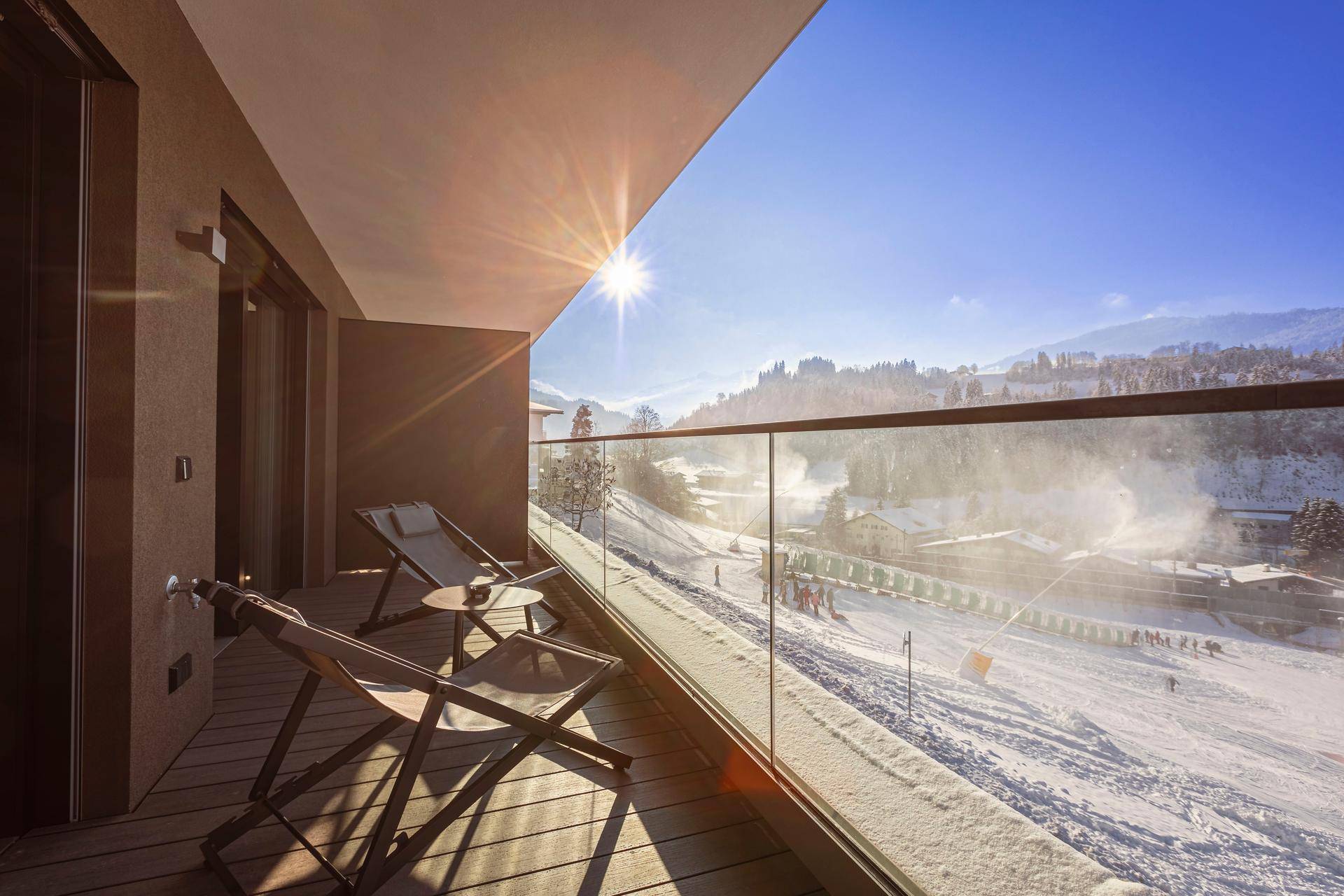 Sonniger Balkon im Winter mit Schnee und Liegestühlen, bietet einen atemberaubenden Blick auf die Skipiste.