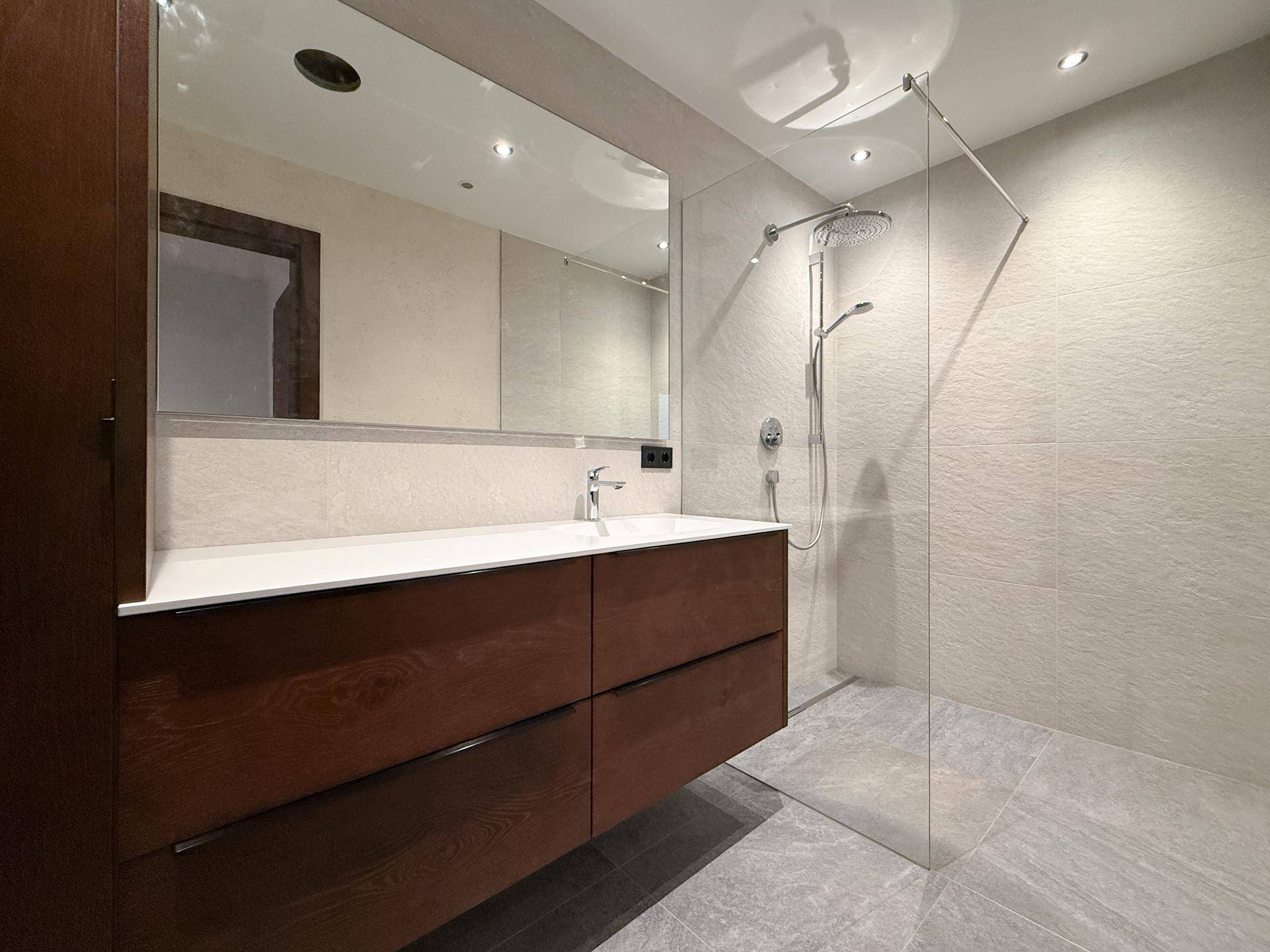 Modernes Badezimmer mit großer begehbarer Dusche, schwebendem Waschtisch und großem Spiegel.