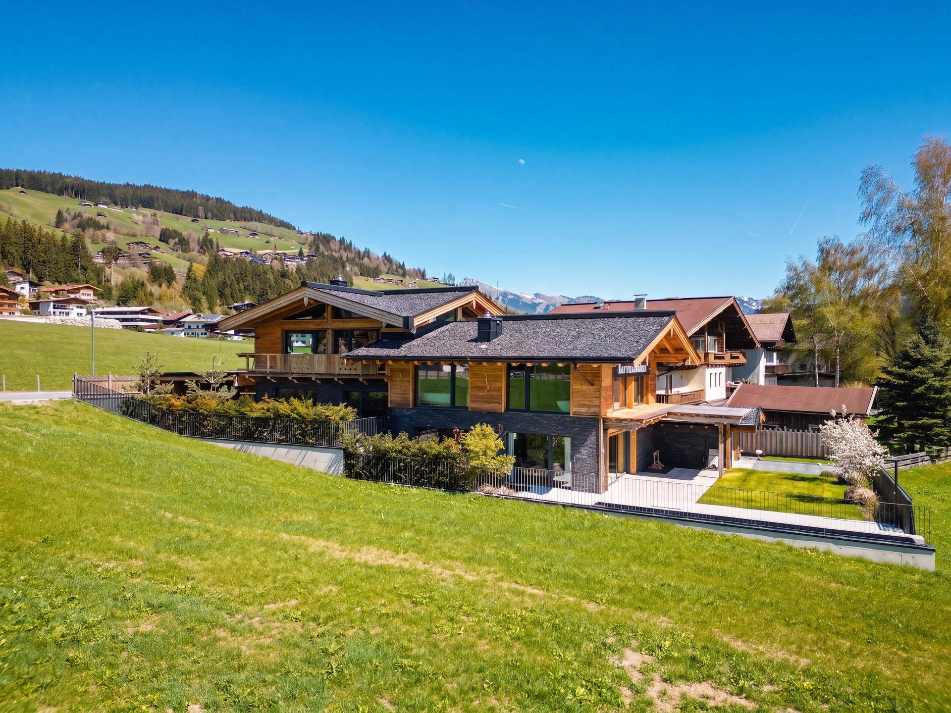 Seitliche Ansicht des modernen Chalet-Hauses mit weitläufigen Grünflächen und Bergblick.