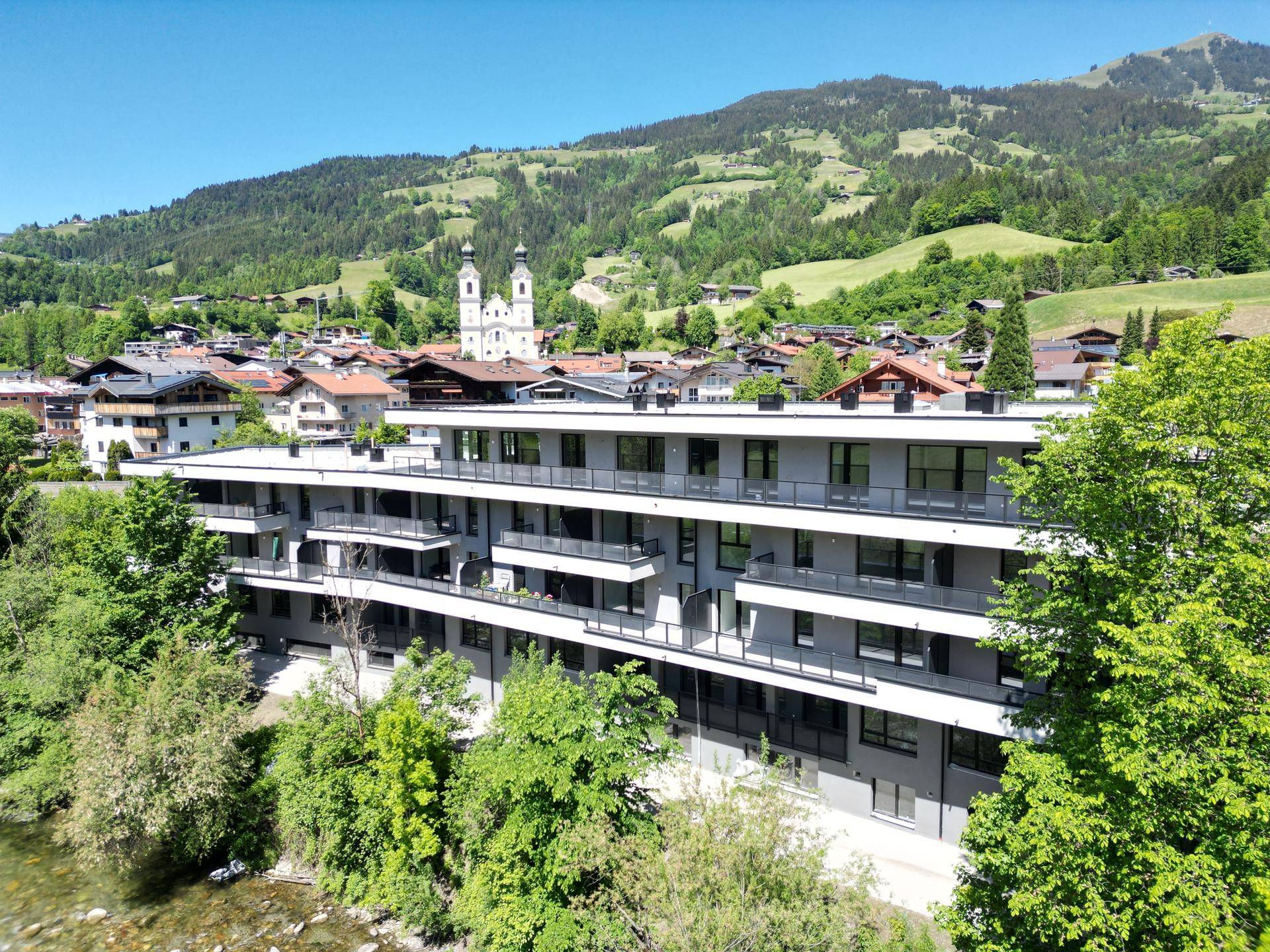 Luftaufnahme eines modernen Gebäudes in einer Berglandschaft mit Fluss und Dorf im Hintergrund.