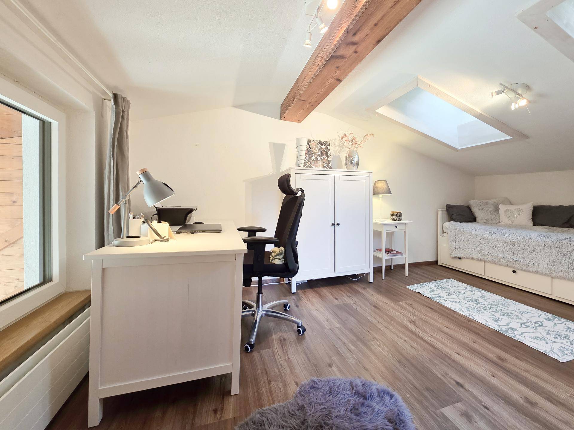 Helles Arbeitszimmer im Dachgeschoss mit Schreibtisch, Tagesbett und Dachfenster.