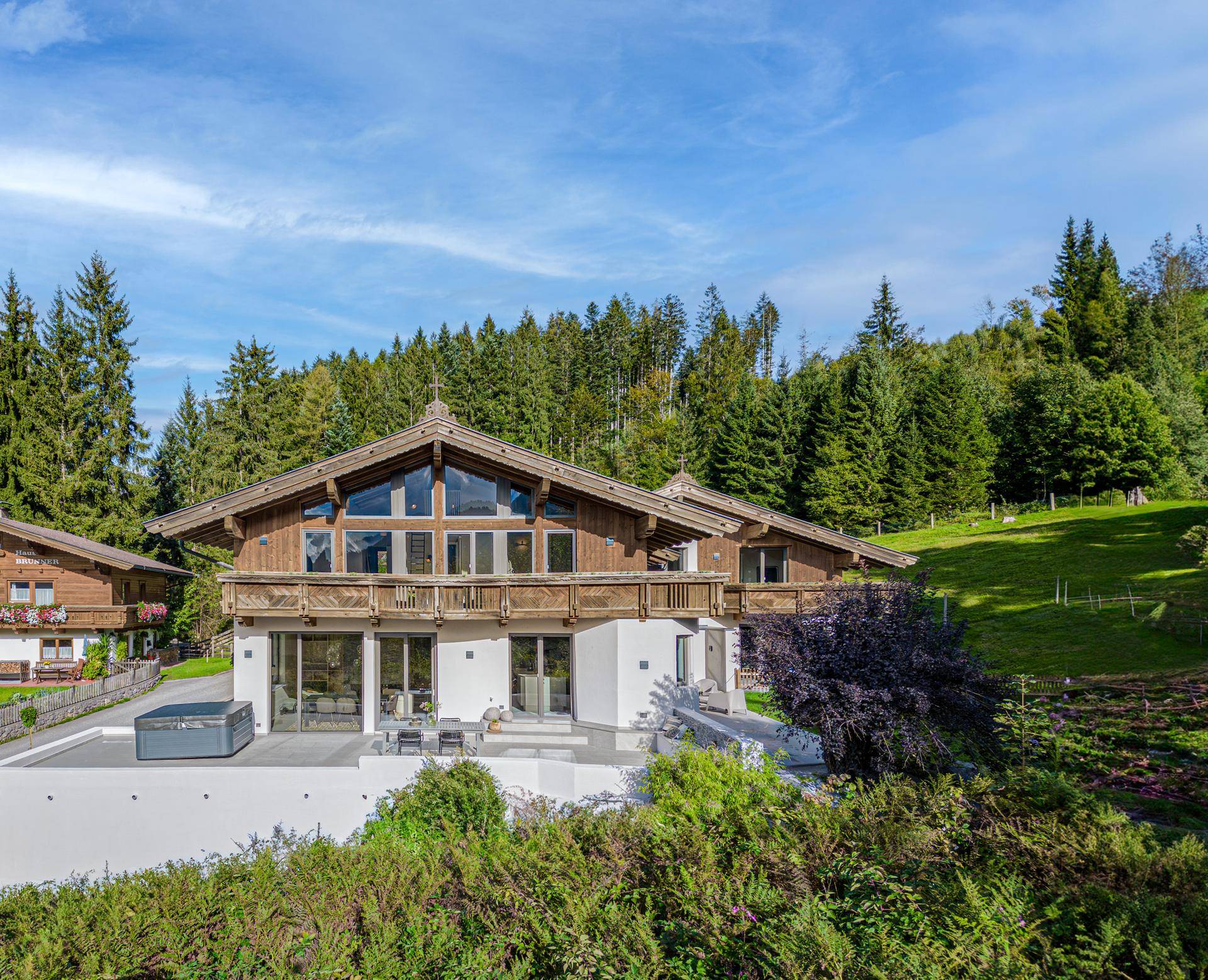 Beeindruckendes Alpenchalet mit großer Glasfassade, Balkonen und Whirlpool auf der Terrasse.