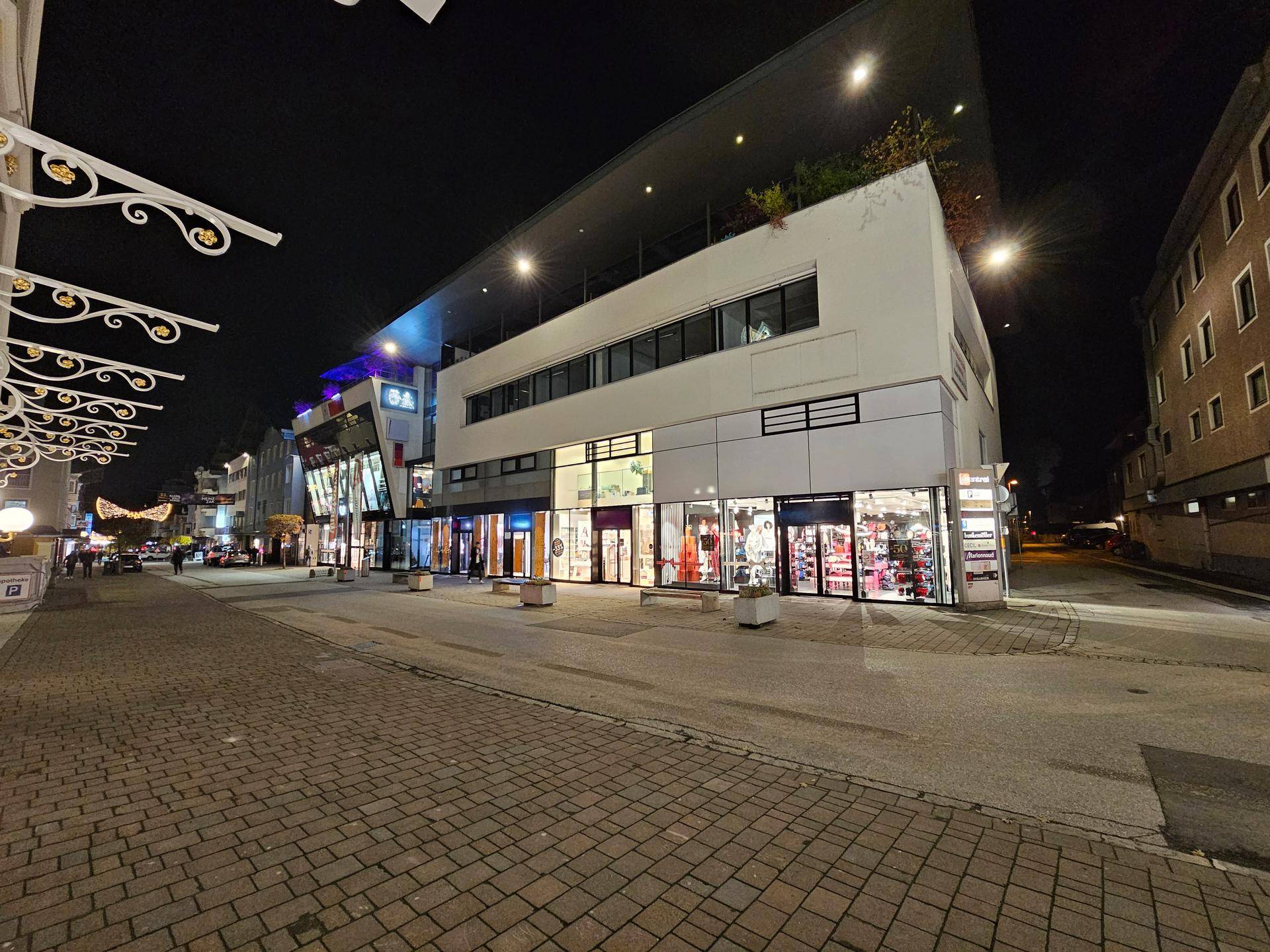 Weitwinkelansicht der modernen Geschäftsfassade bei Nacht mit hell erleuchteten Schaufenstern und dekorativen Elementen.