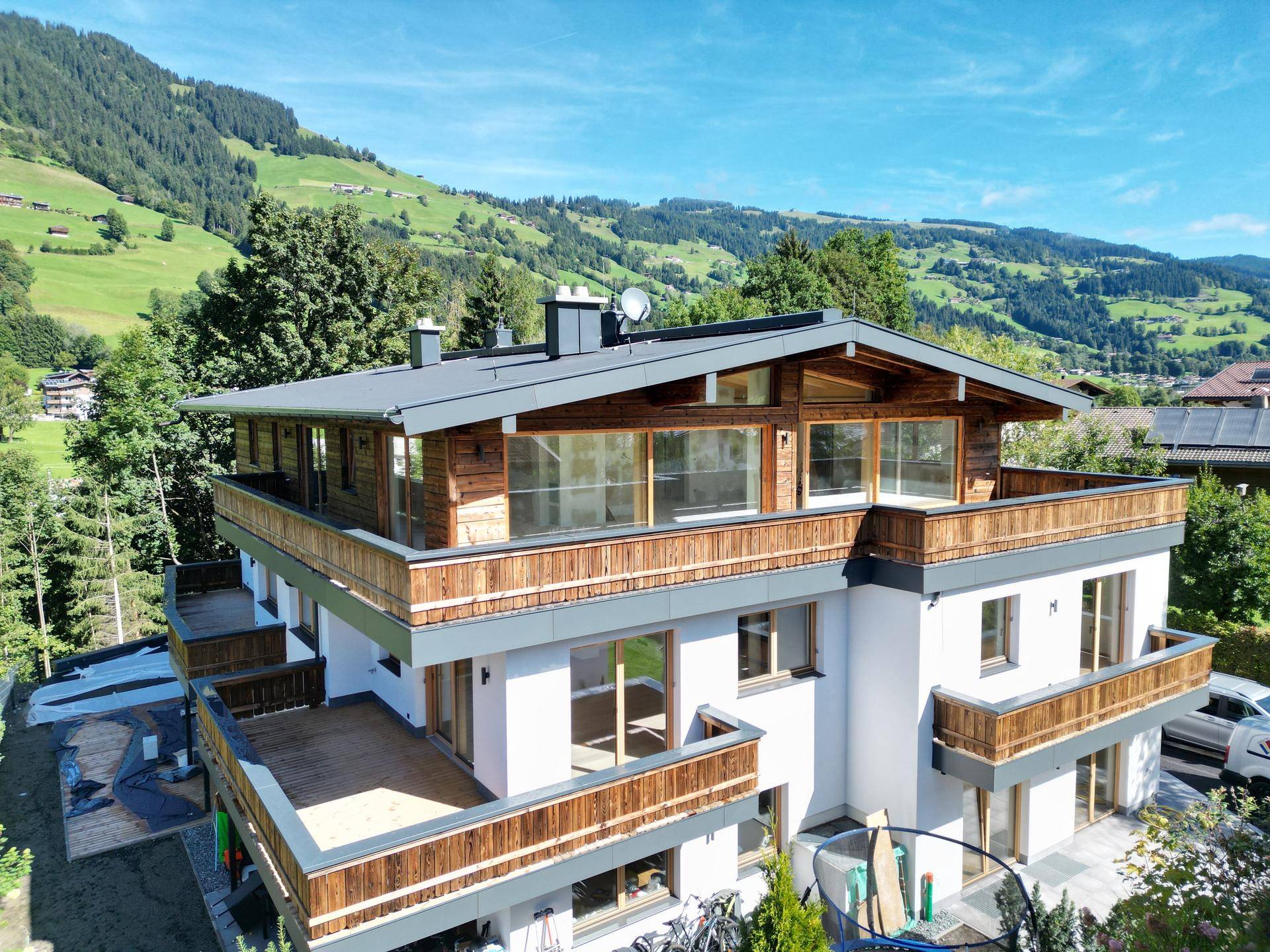 Modernes Holzhaus mit mehreren Balkonen und Terrassen, eingebettet in eine grüne Berglandschaft.